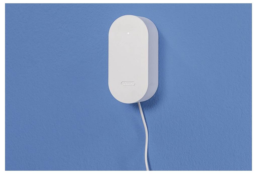 En vit, rektangulär apparat med avrundade kanter är monterad på en blå vägg, med en kabel som hänger nedanför.