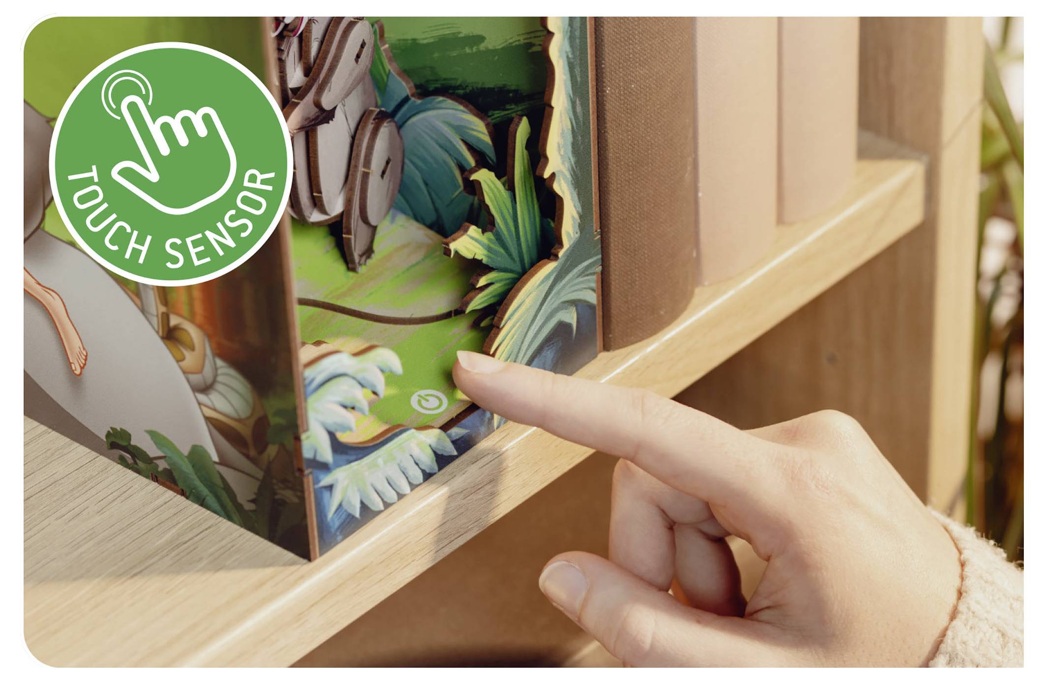 En hand som rör vid en 'Touch Sensor' på sidan av en bok med en grön etikett som illustrerar en handikon, på en träbokhylla.
