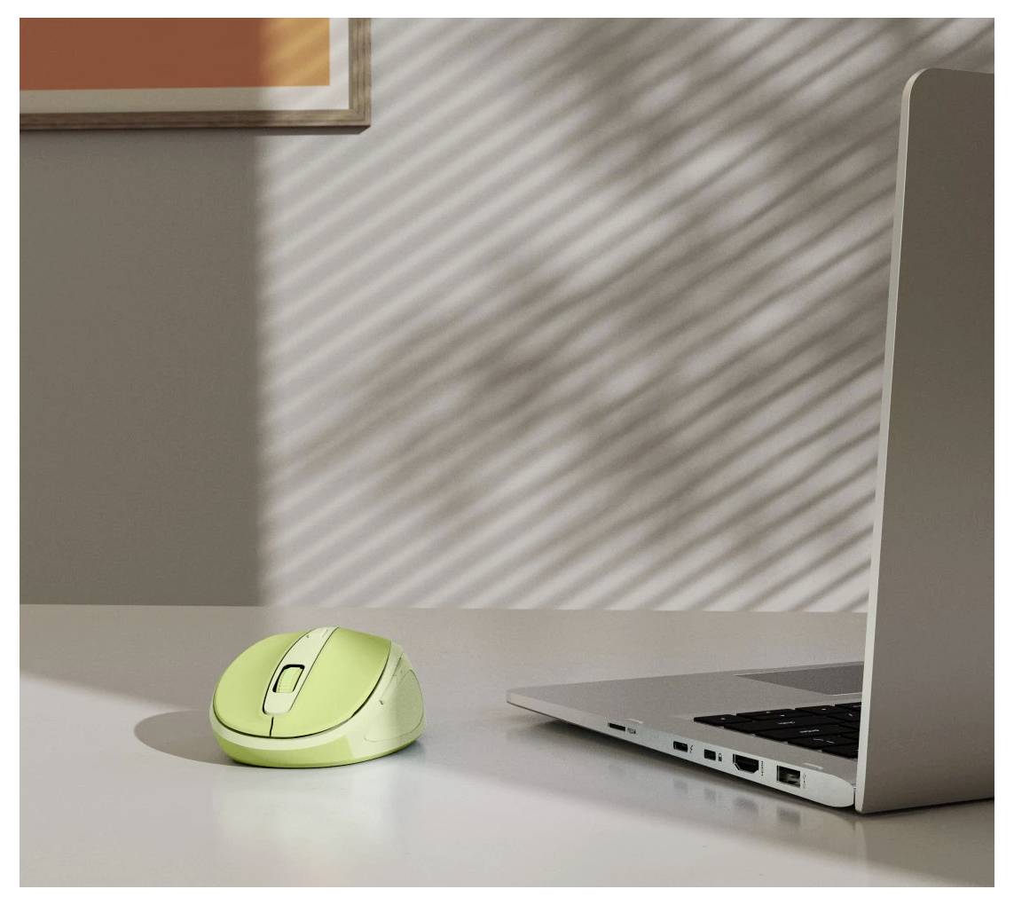 En grön trådlös mus på ett skrivbord bredvid en silver laptop, med solljus som skapar randiga skuggor.