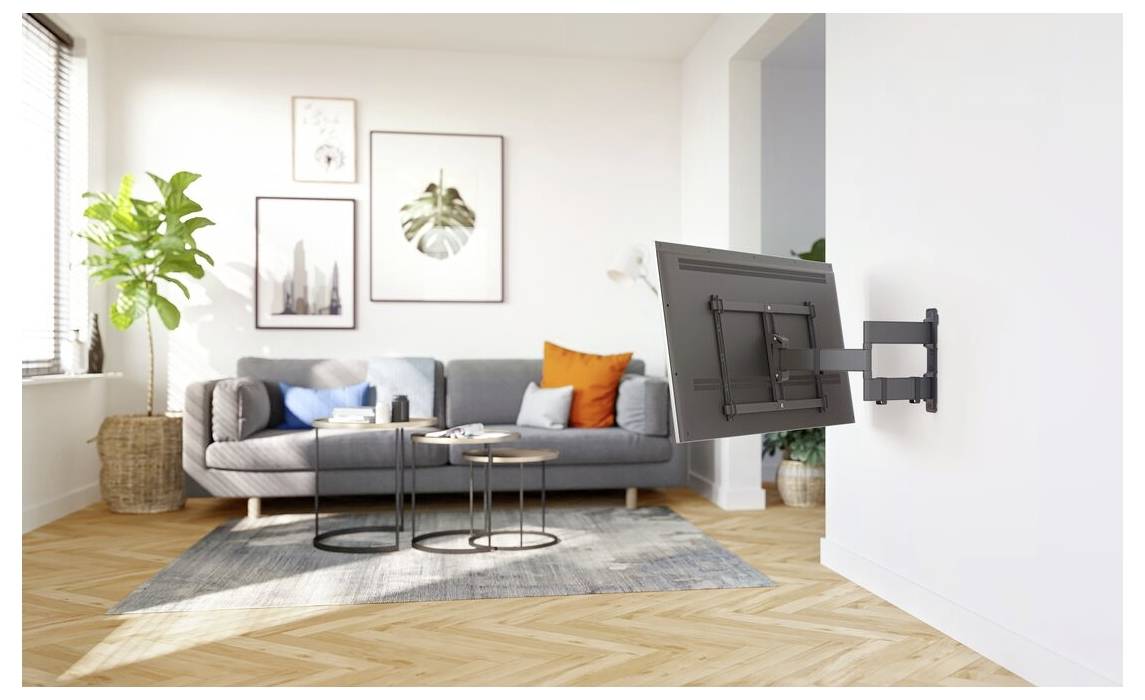 Väggmonterat TV-fäste i vardagsrum. Grå soffa, runda bord och en växt i modern inredning. Solljus genom fönstret framhäver konsten på väggen.
