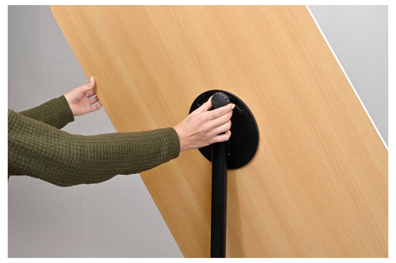 En person i en grön tröja vrider på en vev på en stor träpanel, möjligen för att justera dess position eller vinkel.