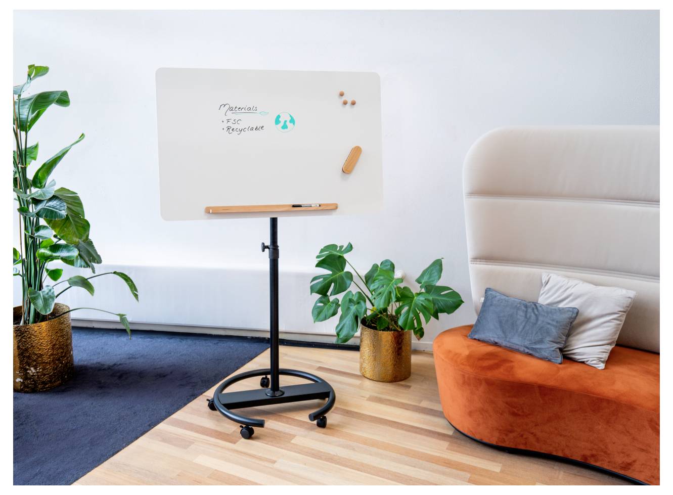 En whiteboardtavla på ett stativ visar texten 'Apotek' och 'Upplevelse' med en blå cirkelformad logotyp. Krukväxter och en orange soffa finns i närheten.