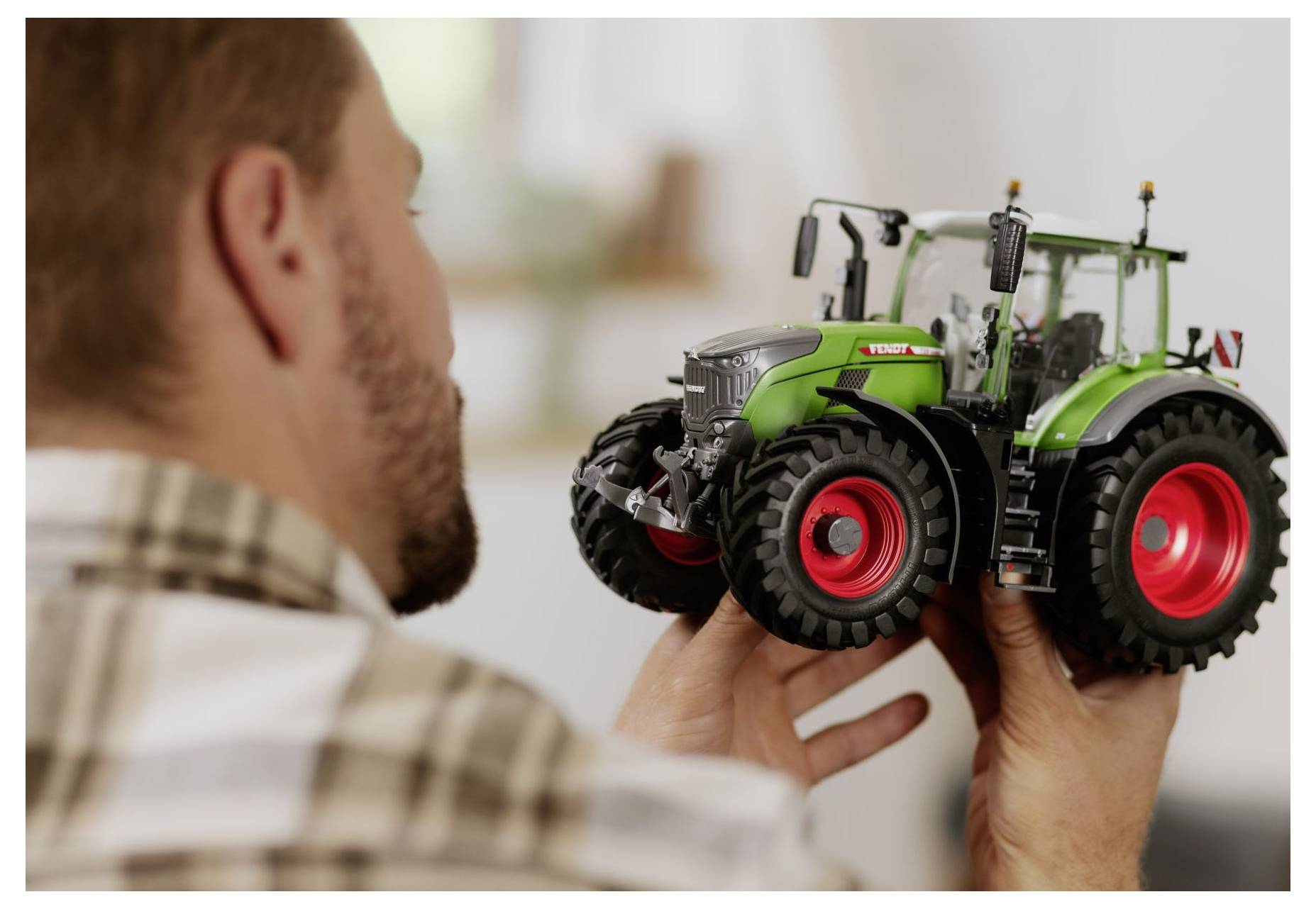 En man håller i en detaljerad modell av en grön och röd traktor och undersöker dess detaljer noga.