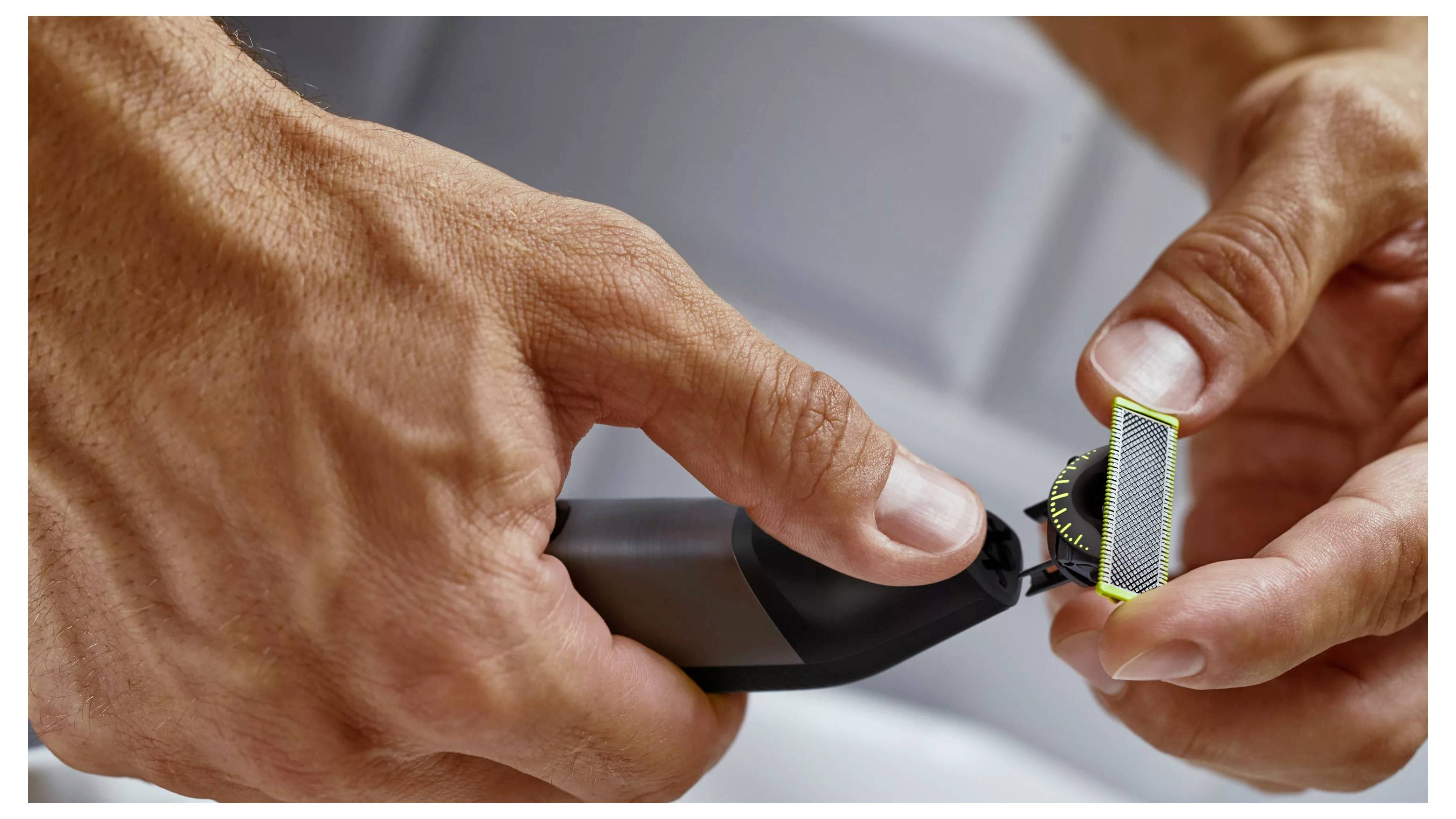 Närbild av händer som håller en rakapparat med ett utbytbart blad, vilket belyser precisionen i groominginstrument.