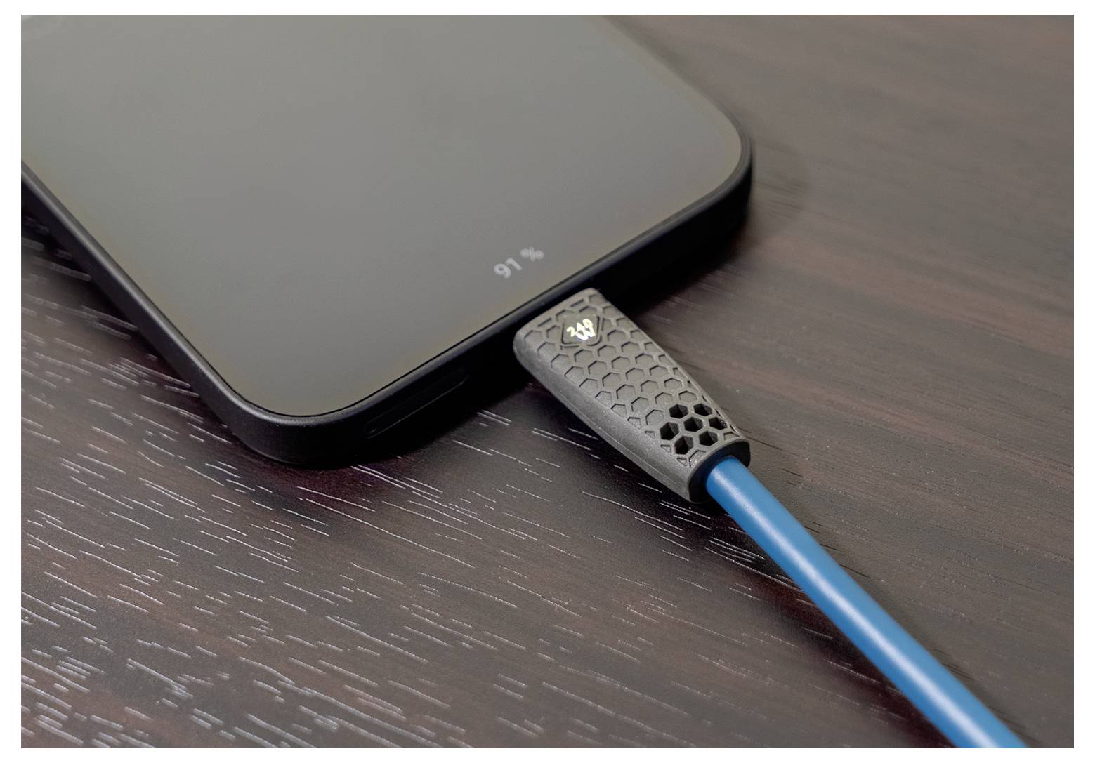 En smarttelefon på ett träbord är ansluten till en strömkälla med en blå laddningskabel, vilket visar att den är laddad till 91%.