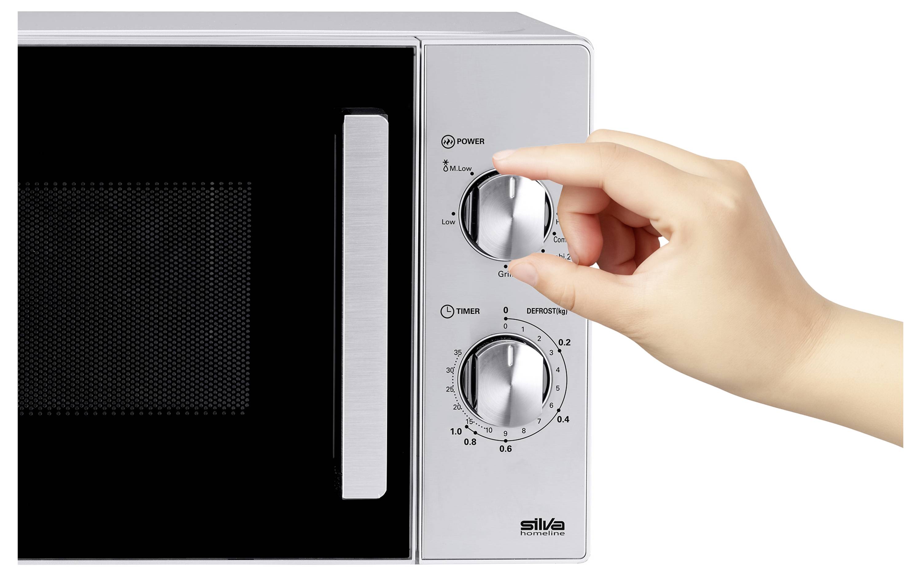 En hand som justerar vredet på en silver mikrovågsugn, med fokus på att ställa in effektnivå och timer.