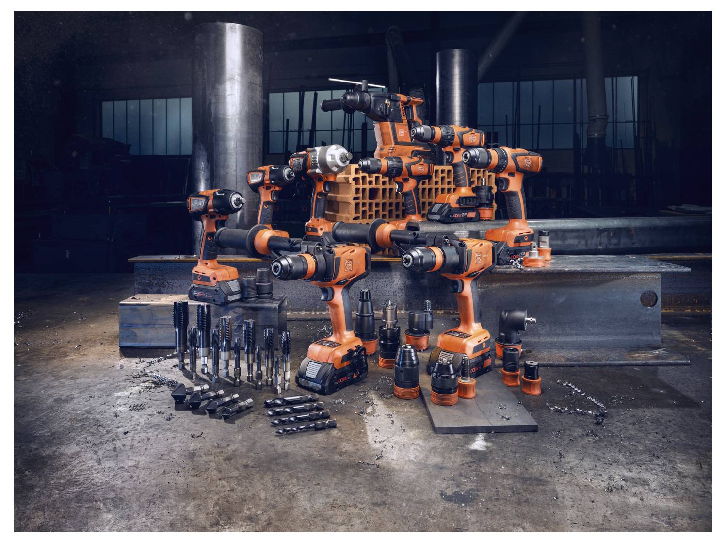 En samling orange och svarta elverktyg är kreativt arrangerad för att likna en robot i en industriell miljö med stålbalkar.