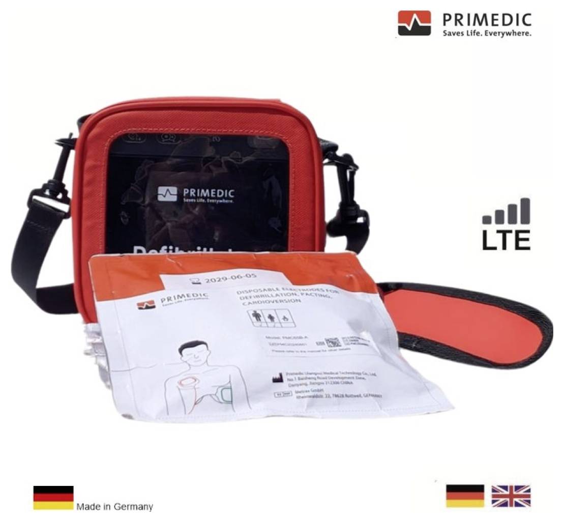En röd defibrillatörkväll med synlig skärm, märkt "PRIMEDIC." Paketet innehåller en manual och är tillverkat i Tyskland. Ikoner visar LTE-anslutning.