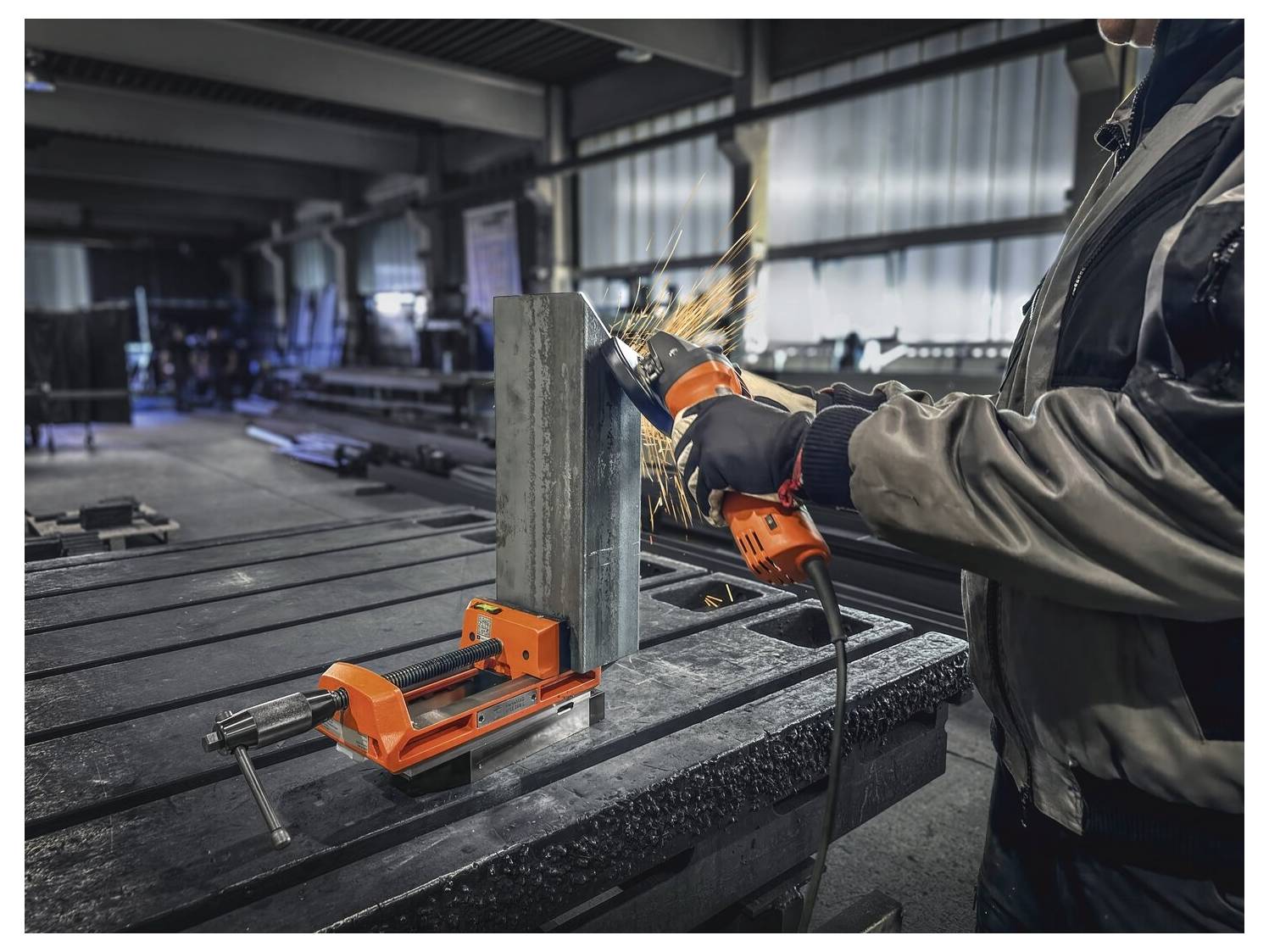 En person använder en vinkelslipad på ett metallblock säkrat i en skruvstäd och skapar gnistor i en industriell verkstadsmiljö.