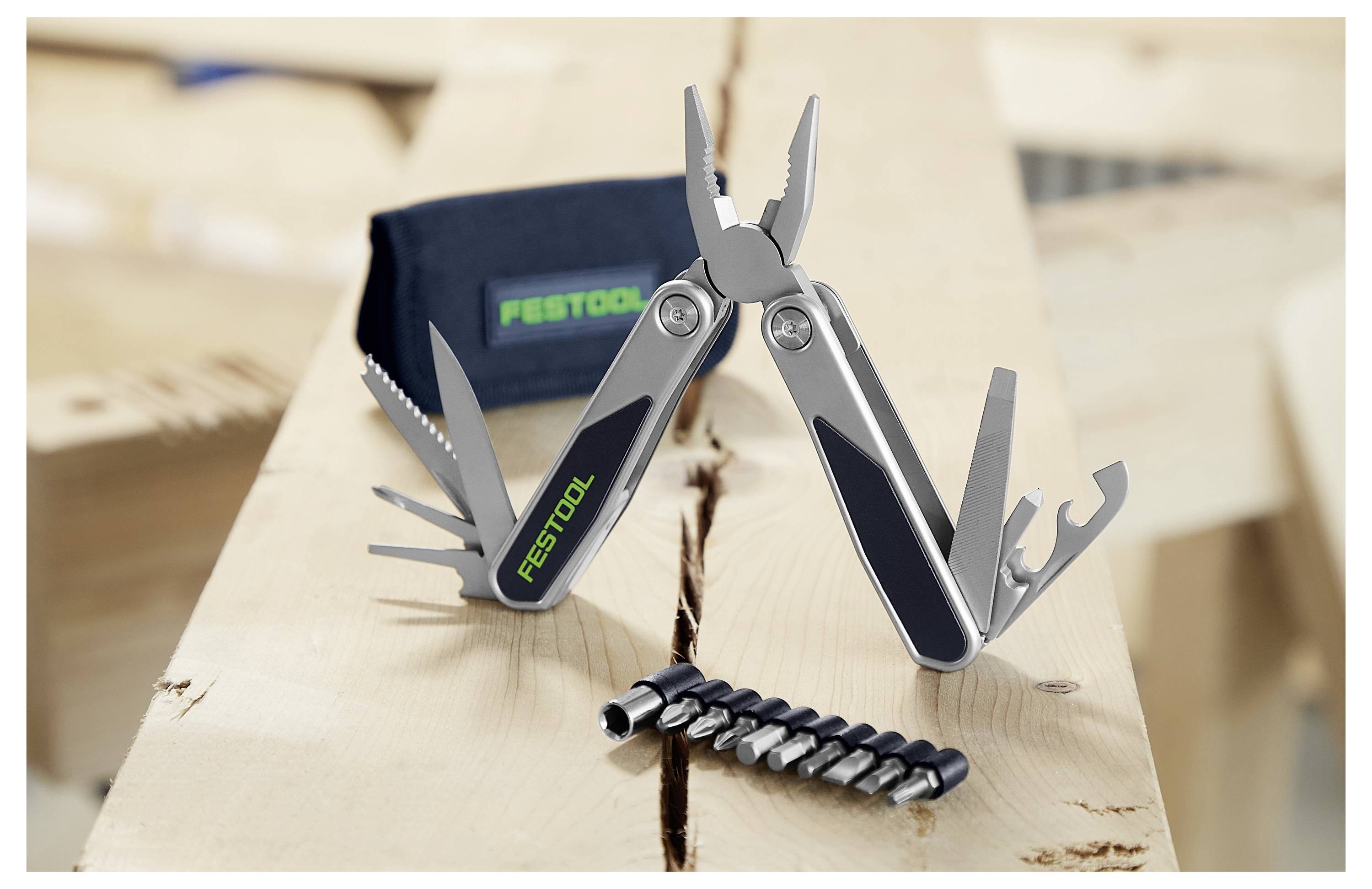 En silver multifunktionsverktyg med olika verktygsdelar öppnade, inklusive tänger och skruvmejslar, på en trä­­yta; Festool-logotyp synlig.