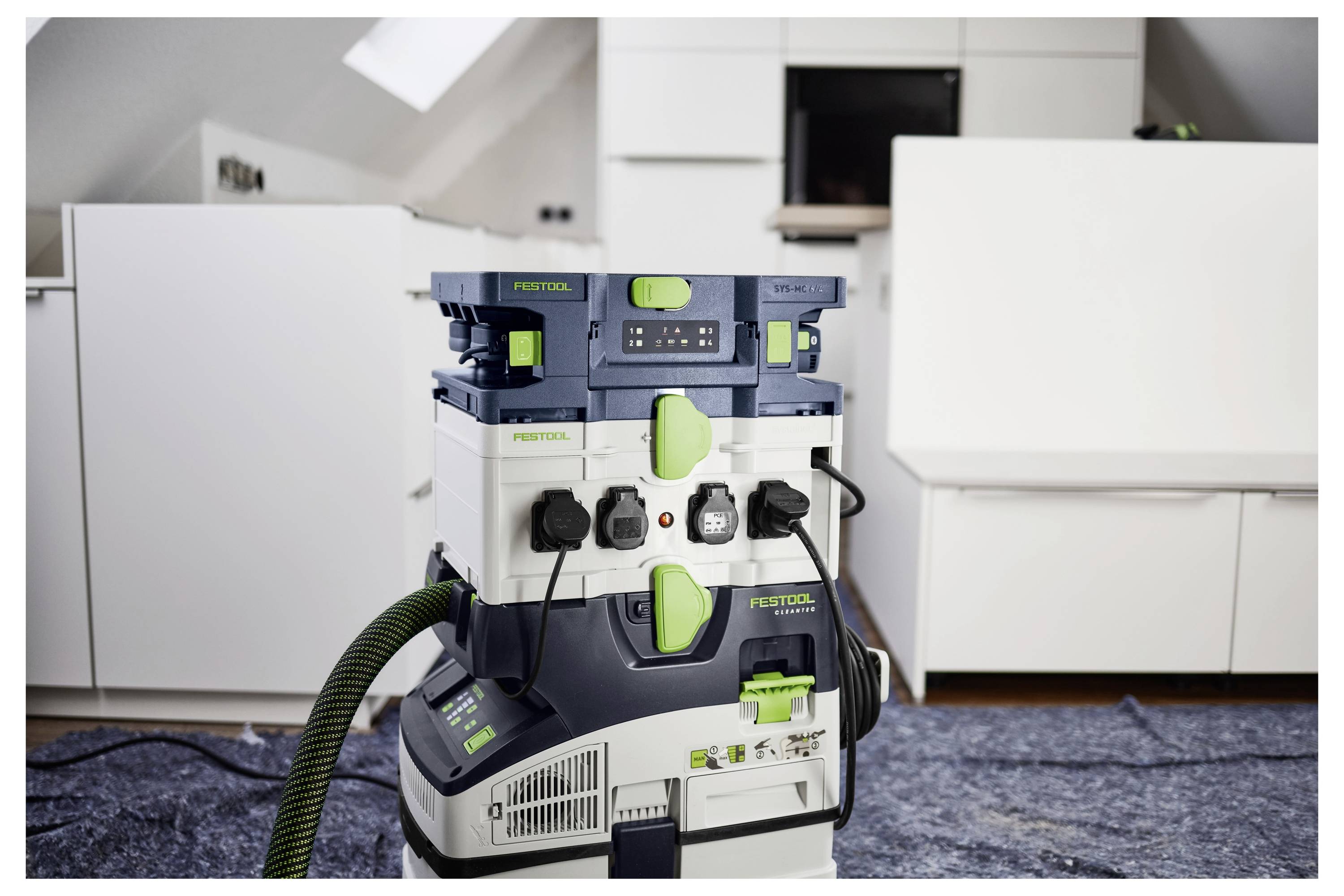 En Festool-dammsugare är placerad på ett blått presenning i en modern, vitt inredningskök omgivet av bänkskivor och minimal dekoration.