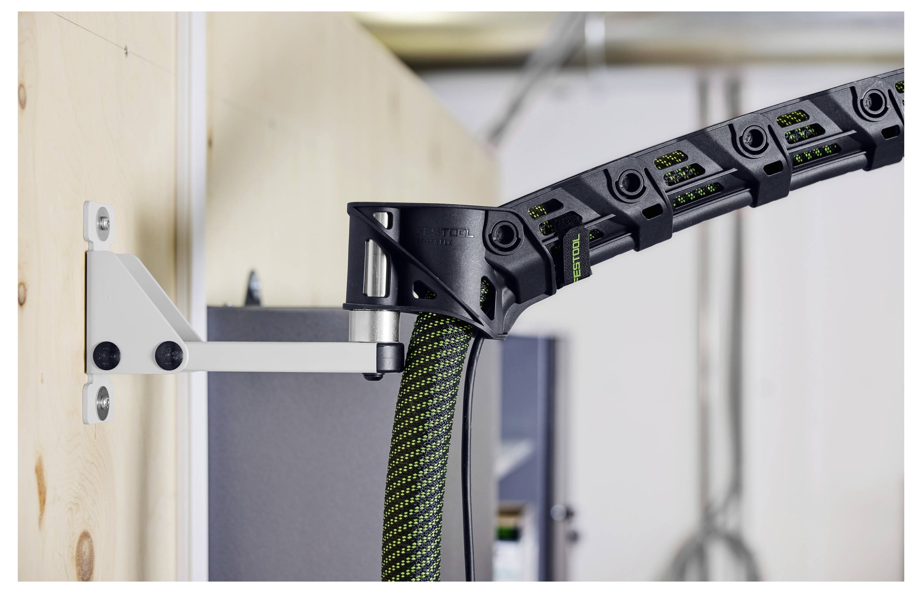 En kabelhanteringssystem fäst på en vägg, som håller en flexibel kabel med gröna och svarta segment, vilket säkerställer organiserad kabelföring.