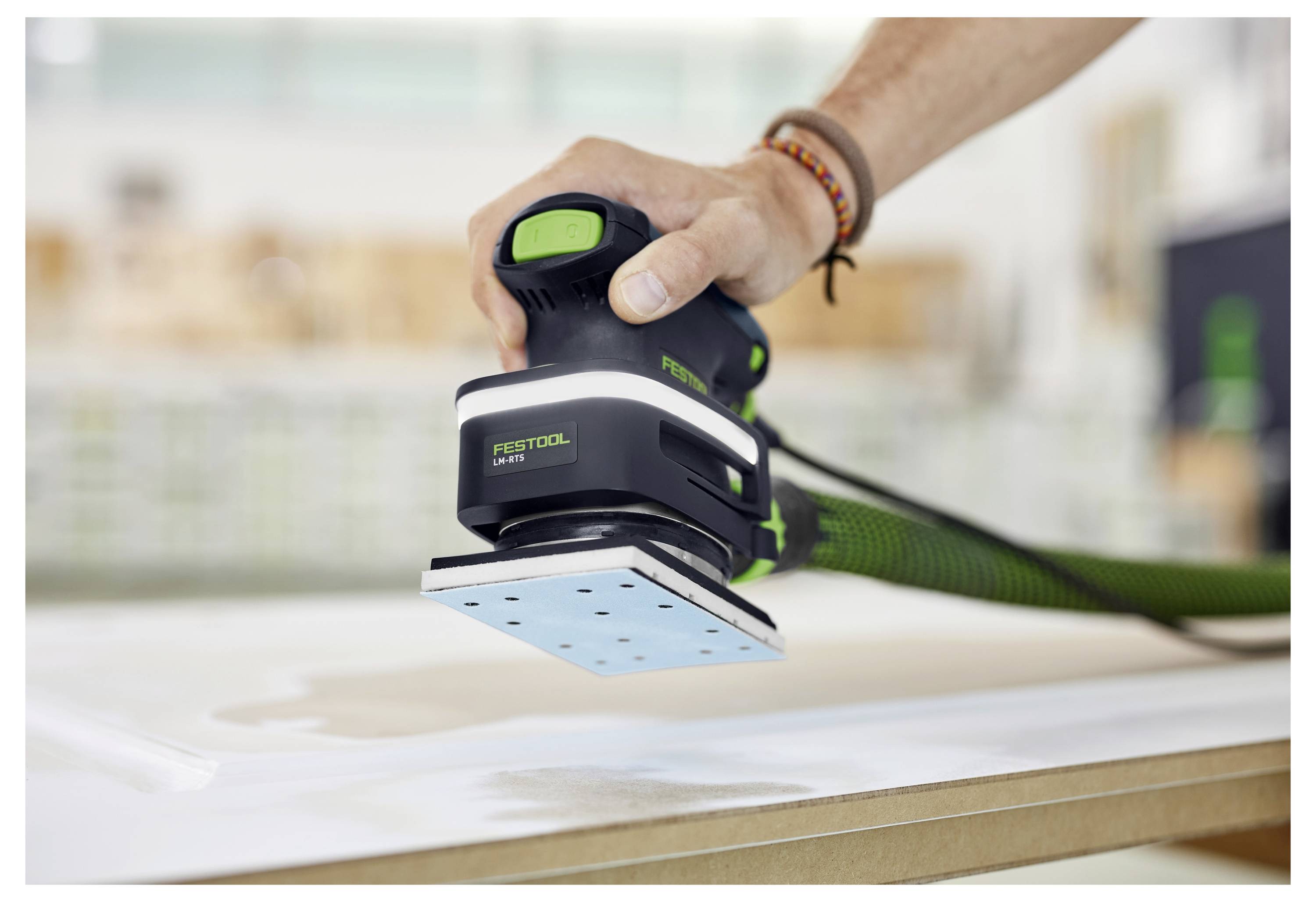 En hand använder en elektrisk slipmaskin för att jämna ut ytan på ett träbräde i en verkstadsmiljö.