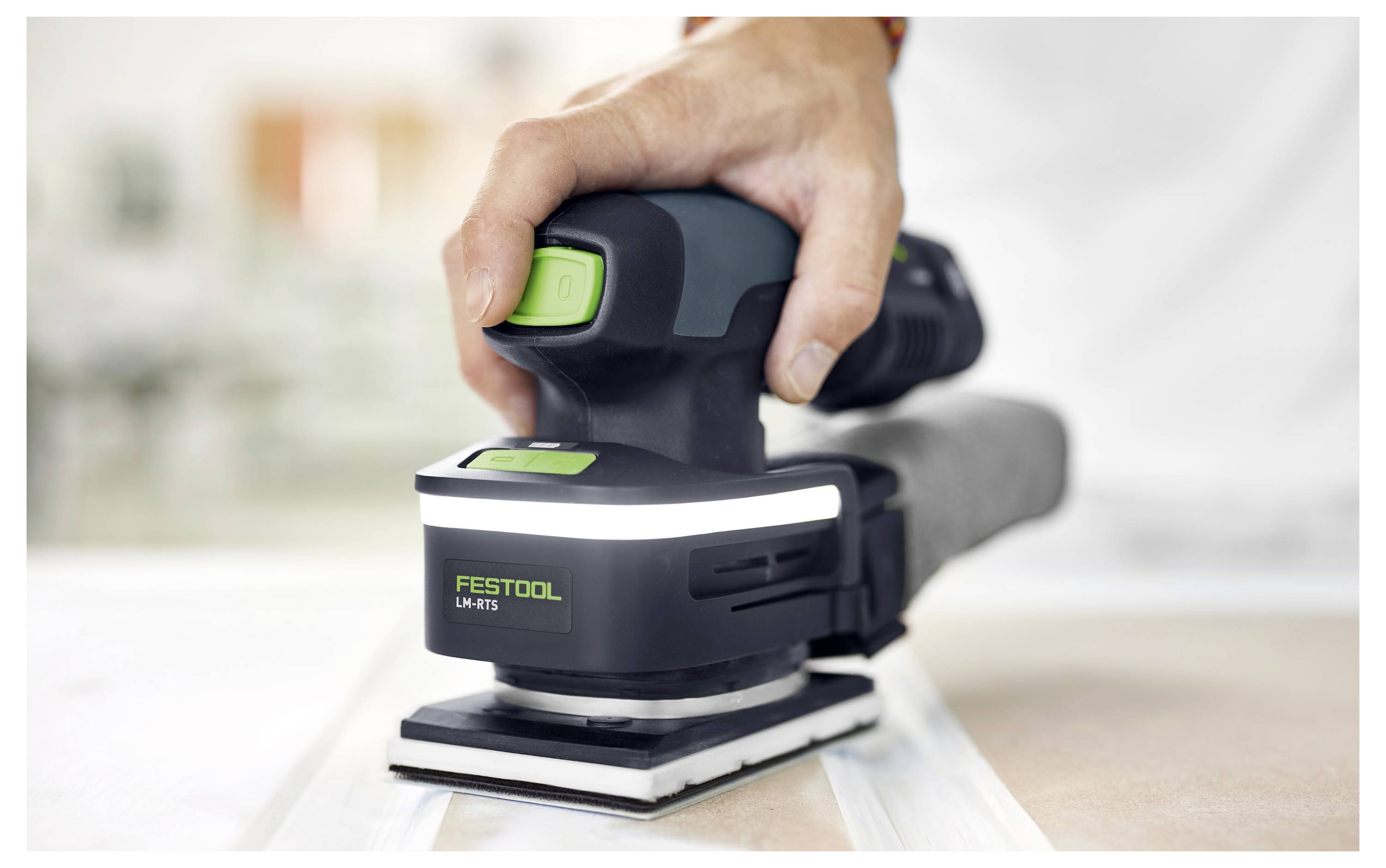 En hand använder en Festool-slipmaskin på en plan yta, som visar dess ergonomiska design och kontrollpunkter, med tonvikt på precision vid slipningsuppgifter.