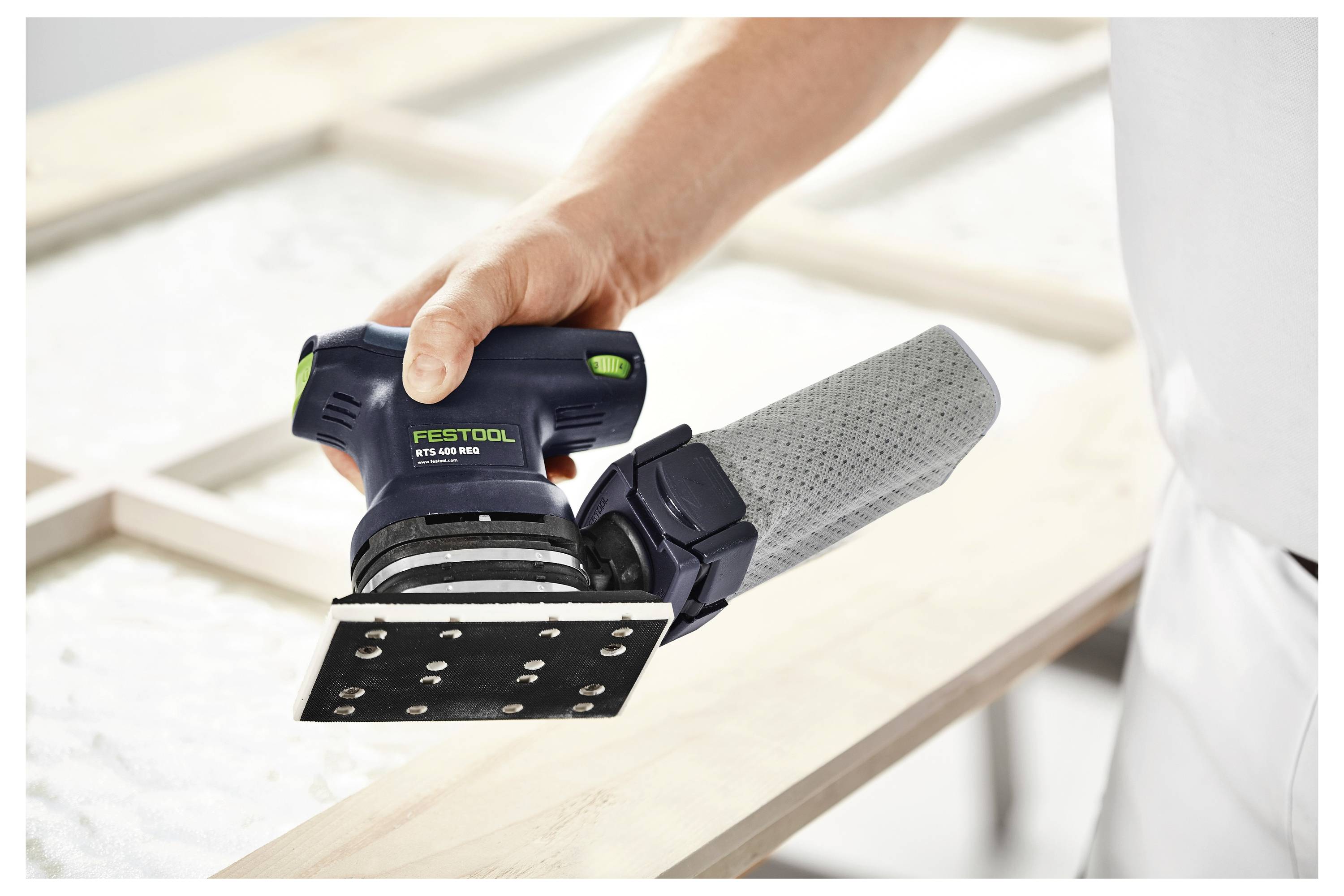 Användare som använder en Festool RTS 400 REQ slipmaskin på en träyta, med fokus på slätt slipning och exakt kontroll.