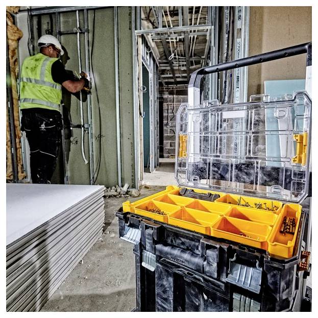 En byggnadsarbetare i en säkerhetväst installerar ledningar i en väggram inuti en byggnad under konstruktion, med en verktygslåda i närheten.