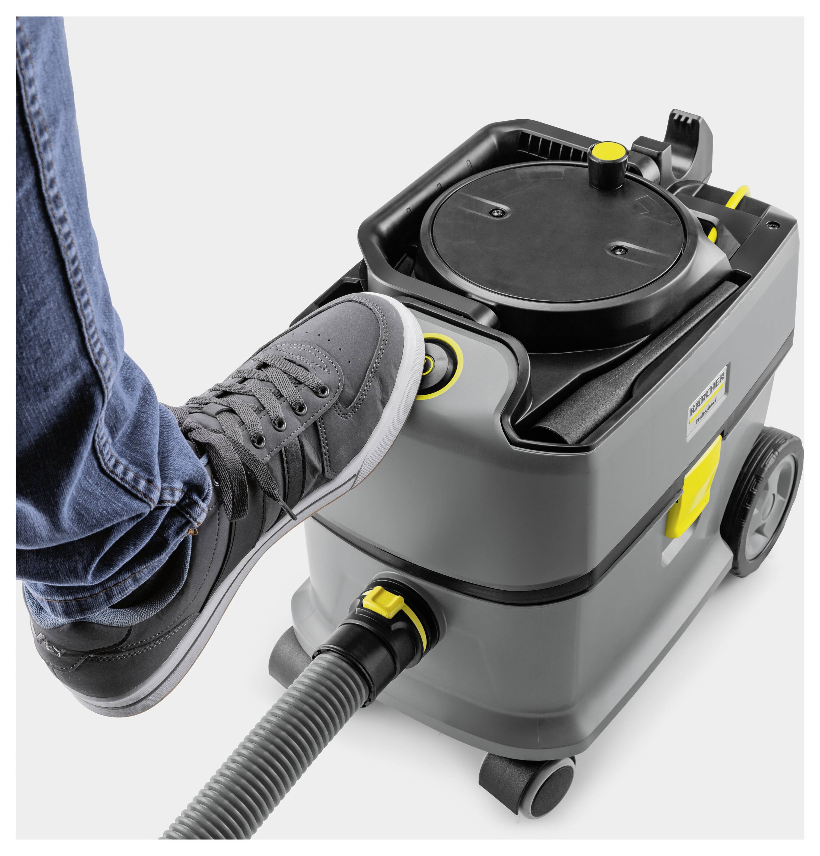 Fot som använder en grå industriell dammsugare med en pedal på toppen, vilket belyser handsfritt bekvämlighet och funktionalitet.