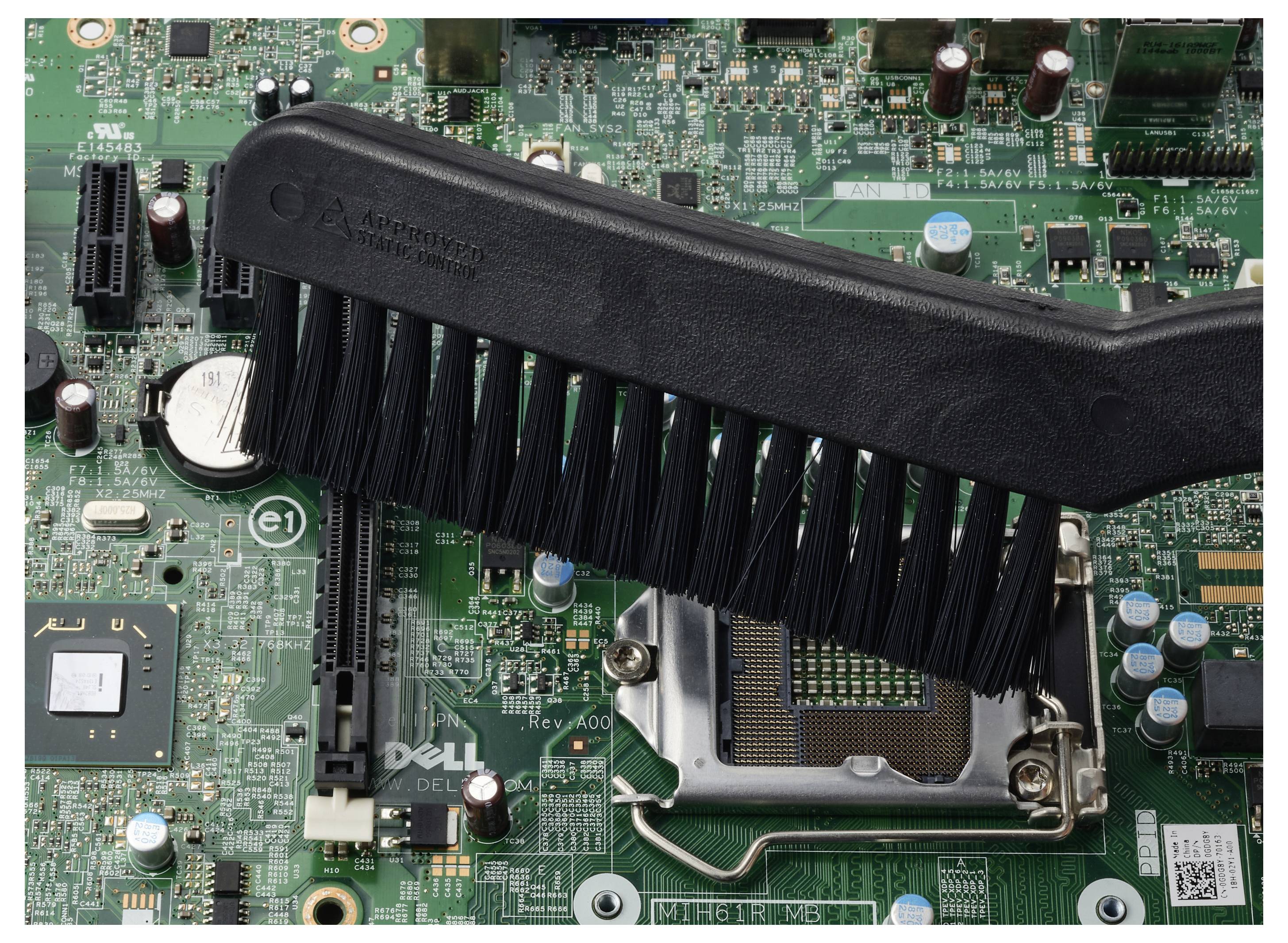 Rengöring av damm från en Dells datormotherboard nära CPU-sockeln och expansionsslotsarna med borste.
