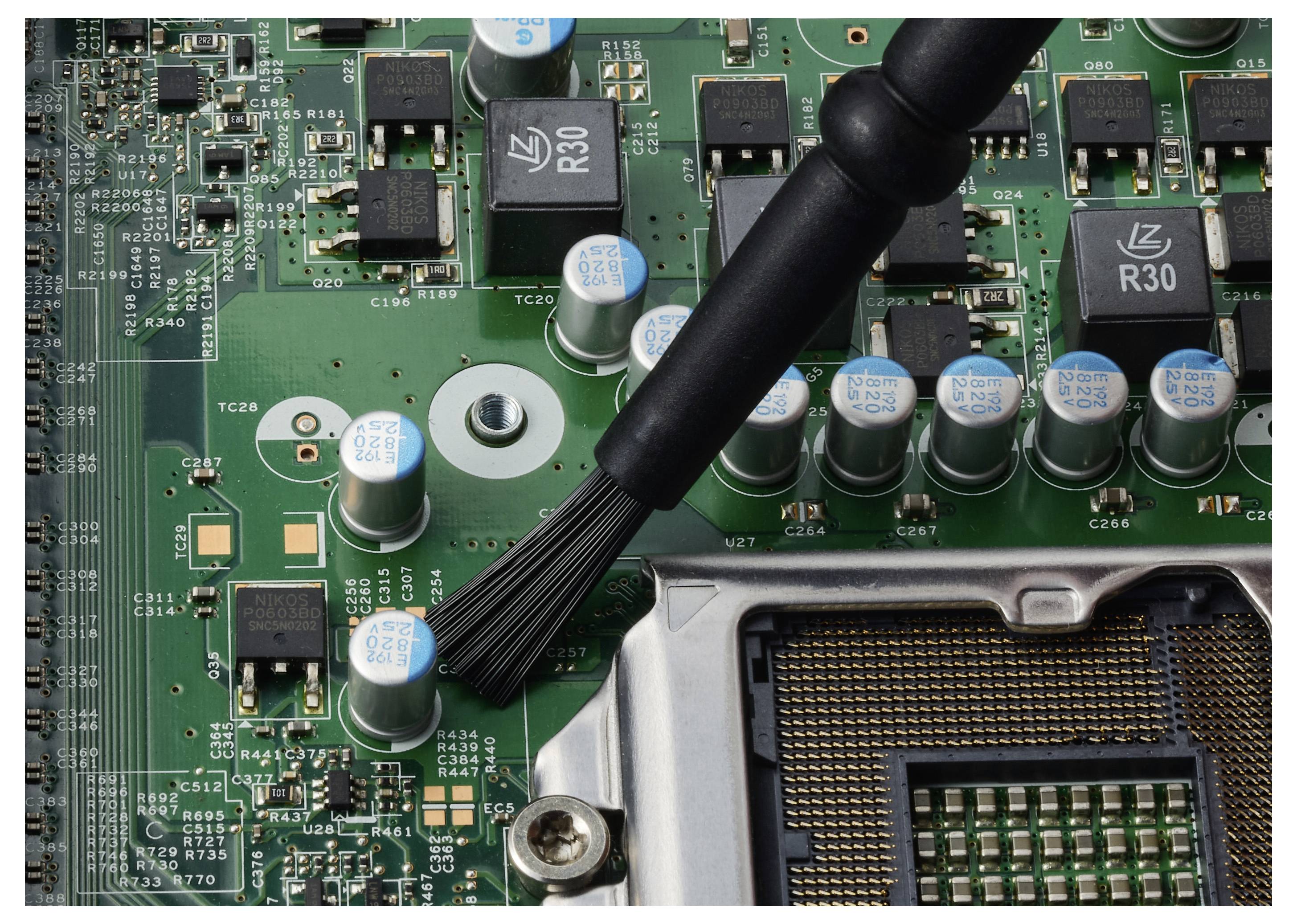 Rengöring av dammpartiklar från ett datorkort nära CPU-sockeln och kondensatorer med en borste.