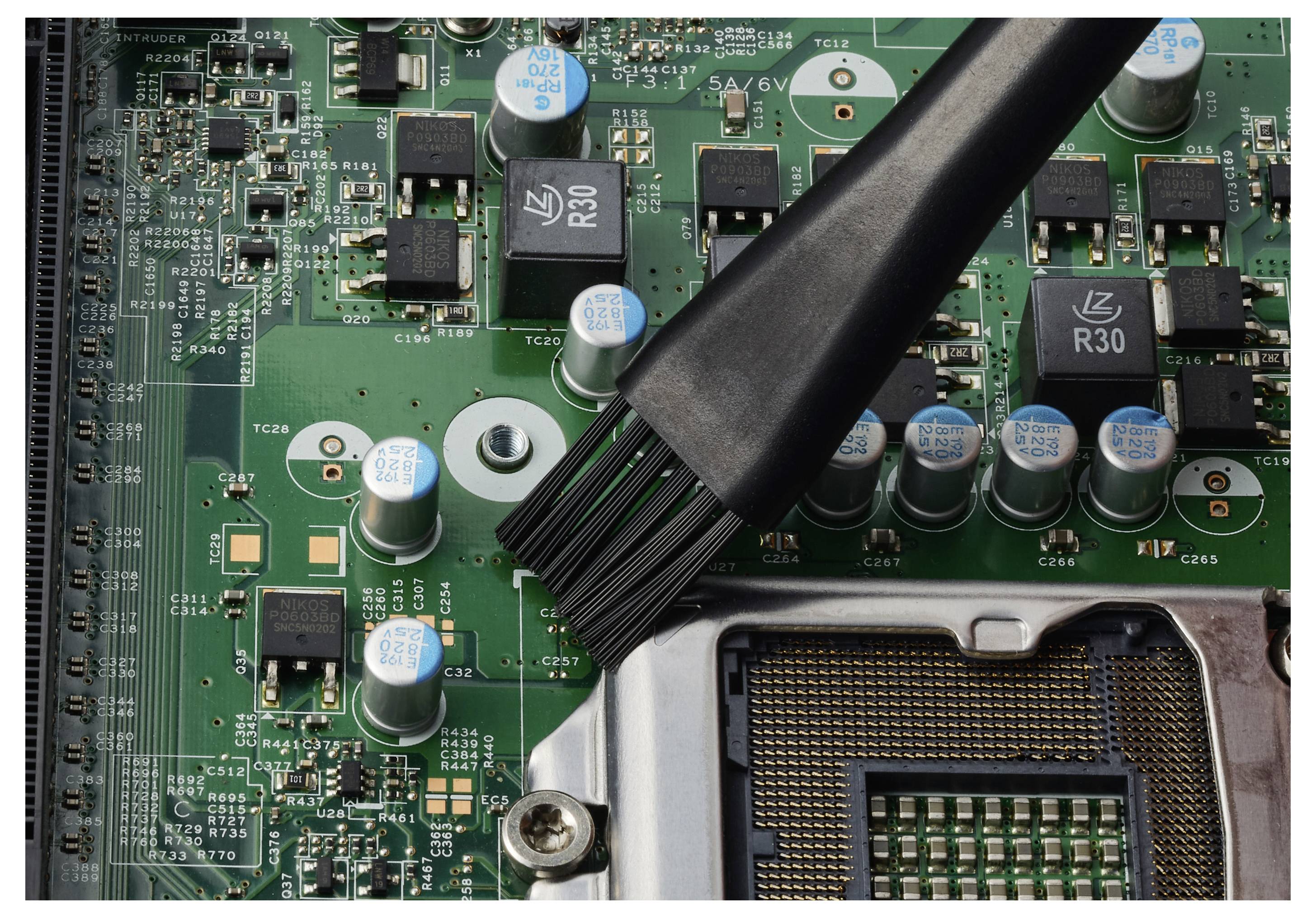 Borsta bort damm från ett datormuterkort nära CPU-sockeln och elektroniska komponenter.