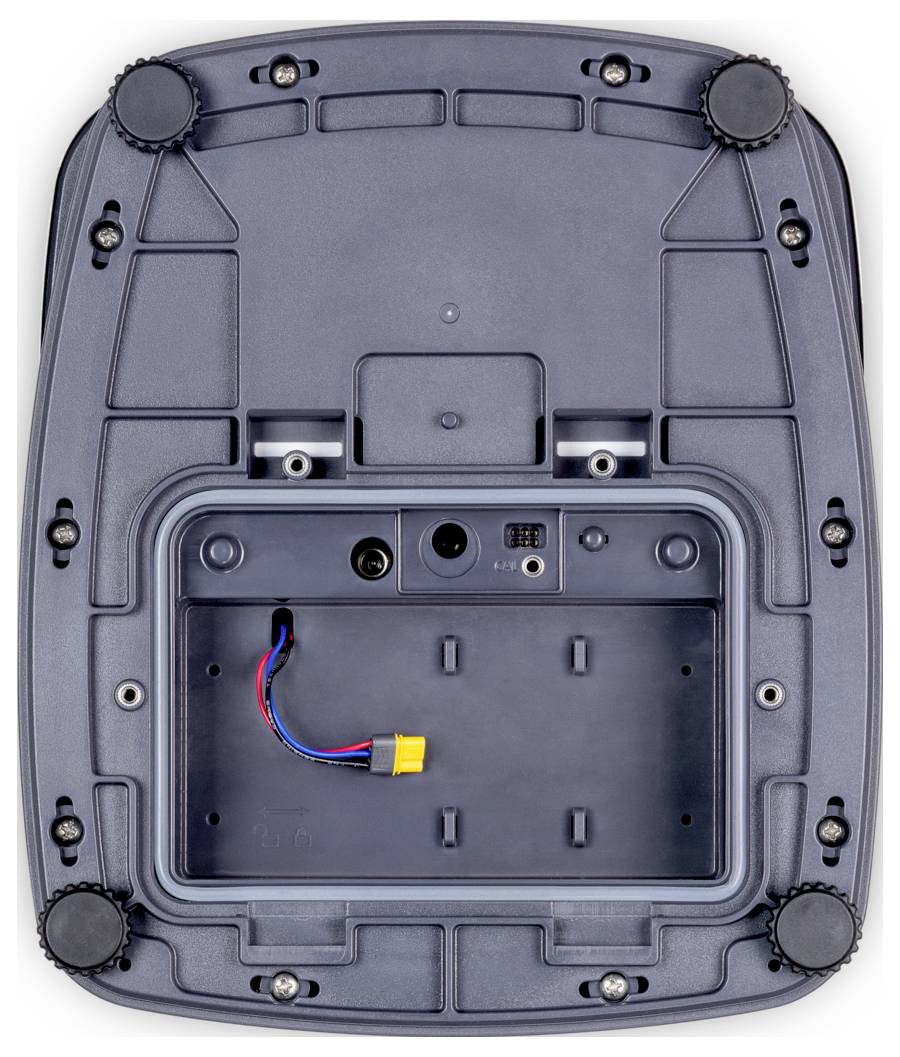 Bilden visar undersidan av en elektronisk enhet med ett fack för ett batteri, flera skruvar och gummifötter för stabilitet.