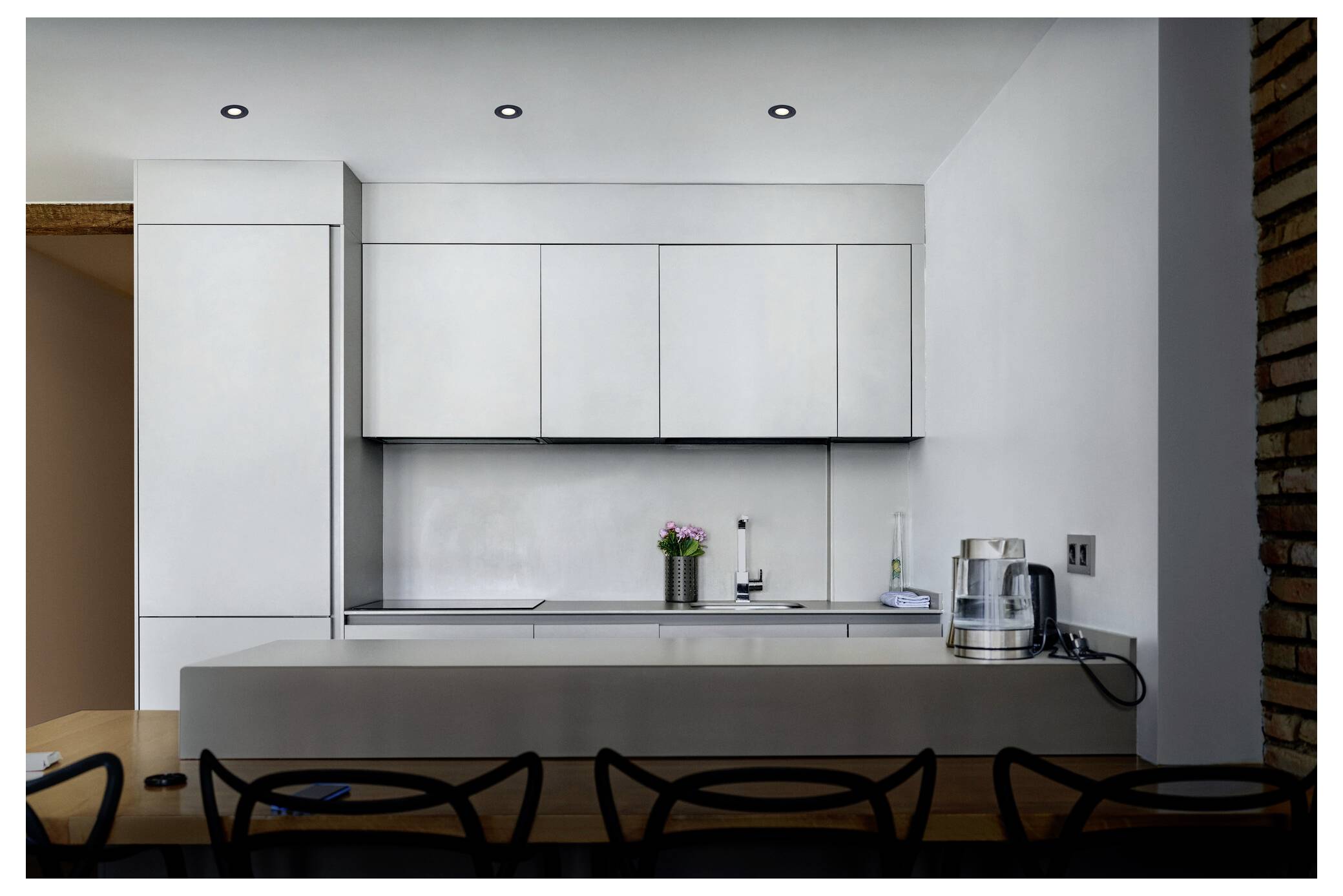 Modernt kök med släta vita skåp, en rostfri vattenkokare och krukväxter på bänken. Minimalistisk design och mjuk belysning.