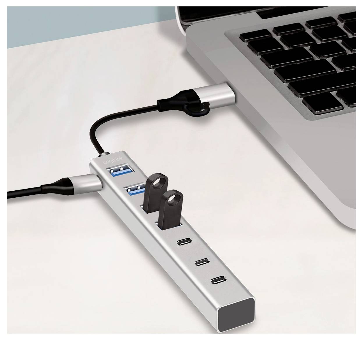 Laptop ansluten till en USB-C-hub med flera USB-portar och strömkabel, som visar utökad anslutningskapacitet på ett skrivbord.