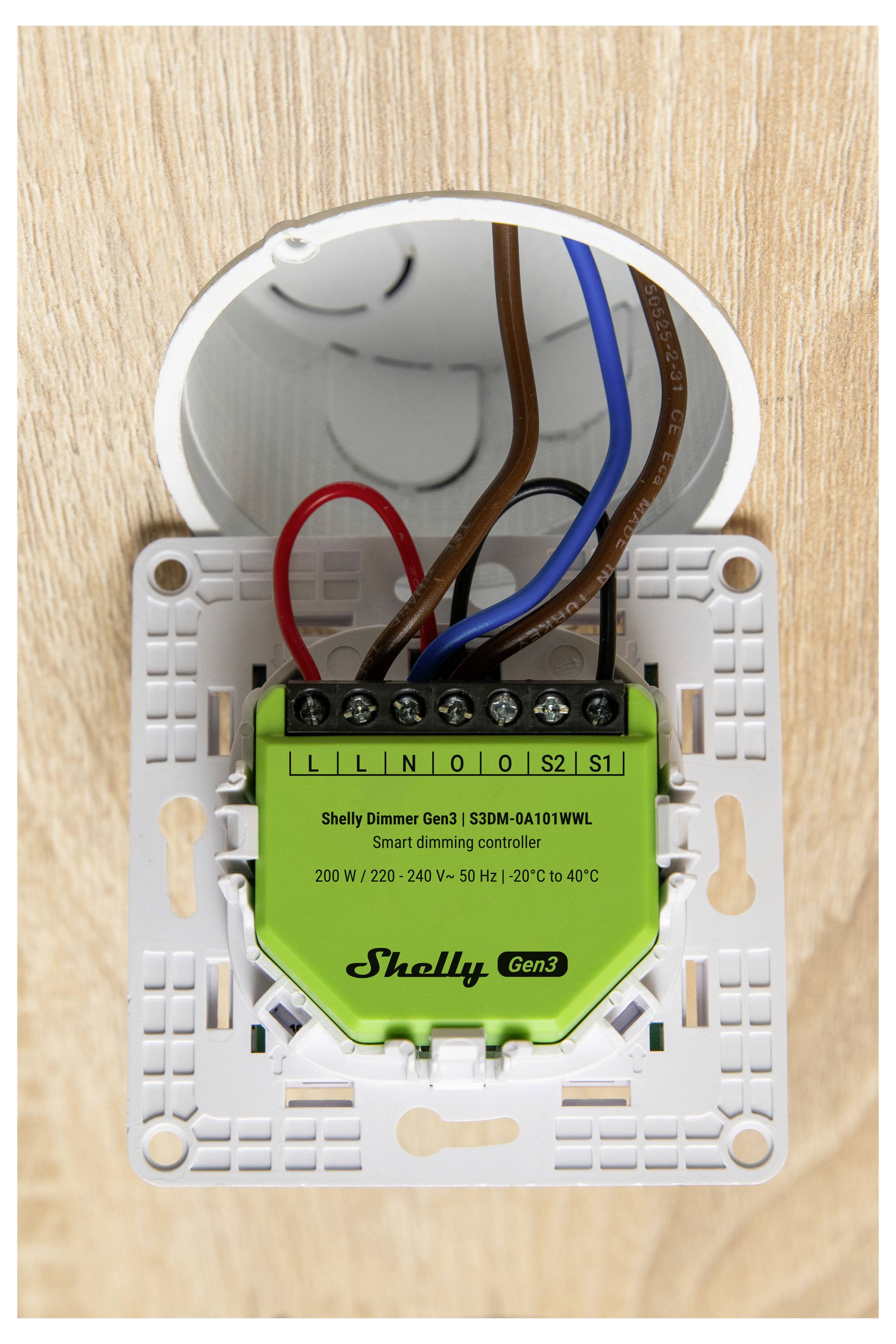 En smart dimreglare installerad i en rund elektricitetslåda. Den är märkt "Shelly Dimmer Gen3" och ansluten med röda, blå och bruna ledningar.