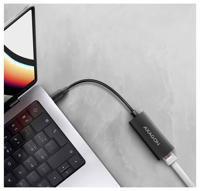 Bärbar dator ansluten till en AXAGON USB-C-adapter/dongel på en grå yta.