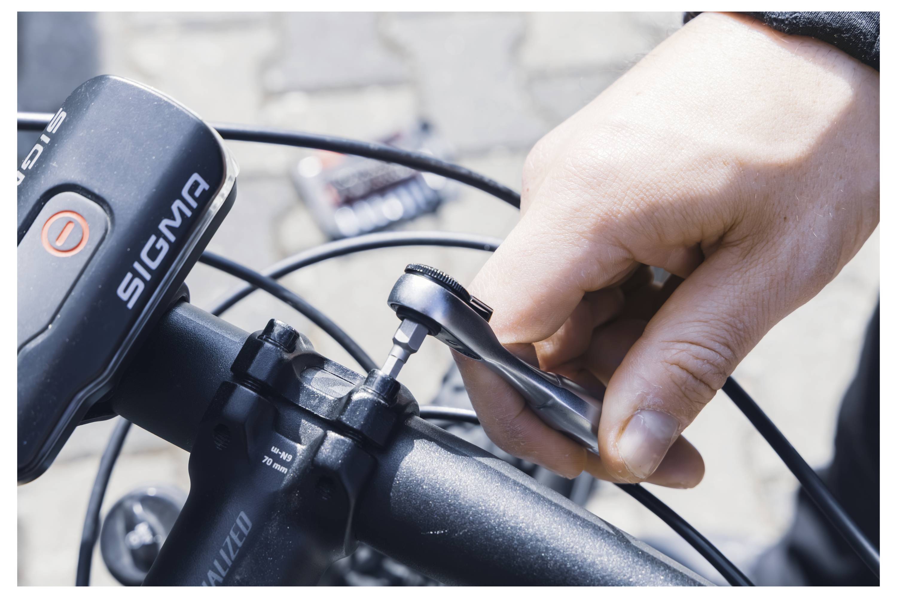 En person drar åt en skruv på ett cykelstyre med en inbussnyckel. Cykeln har en Sigma cykeldator monterad.
