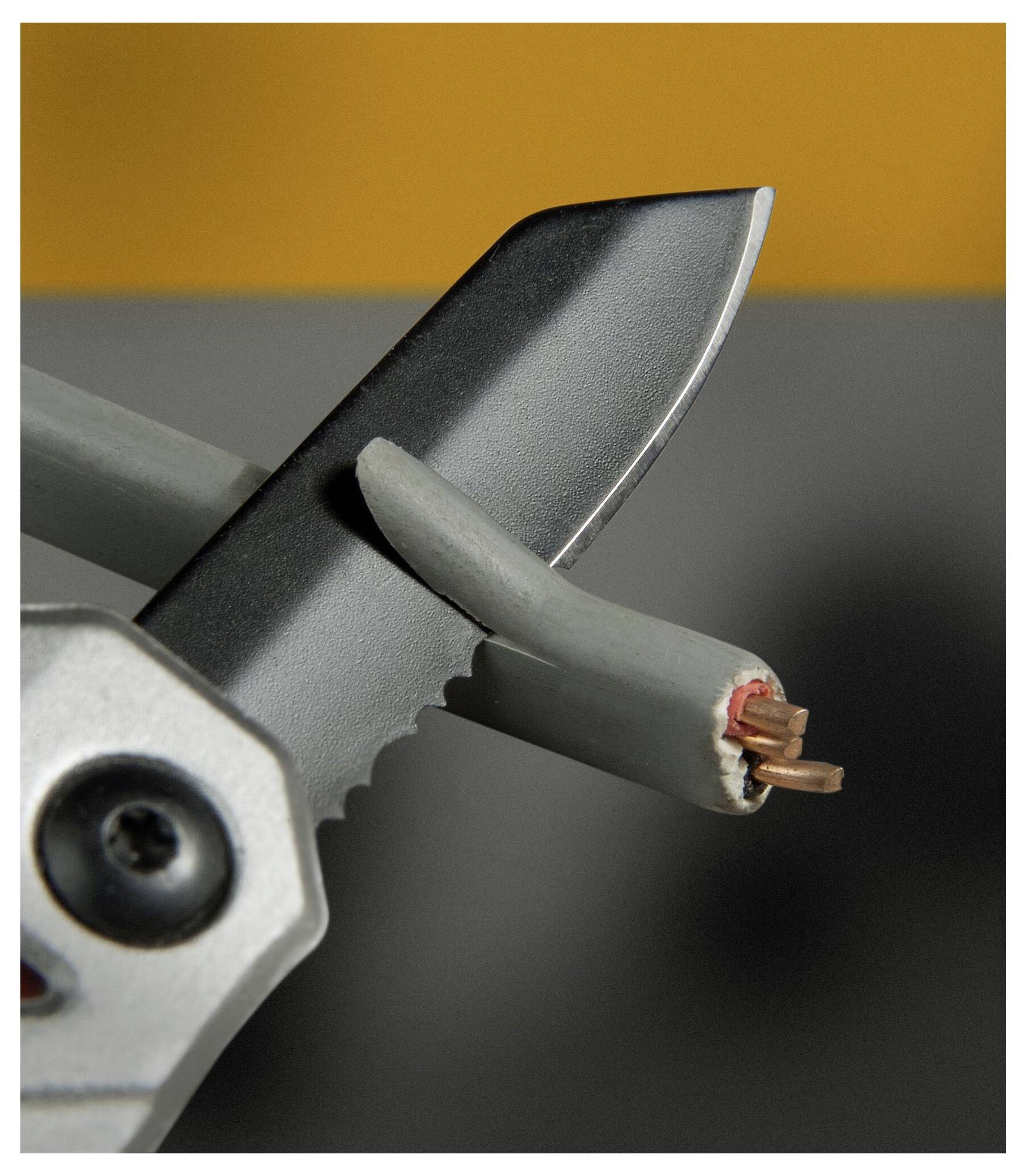 En närbild av en tång som klipper genom en grå elektrisk kabel och exponerar koppartrådar, mot en suddig orange och grå bakgrund.