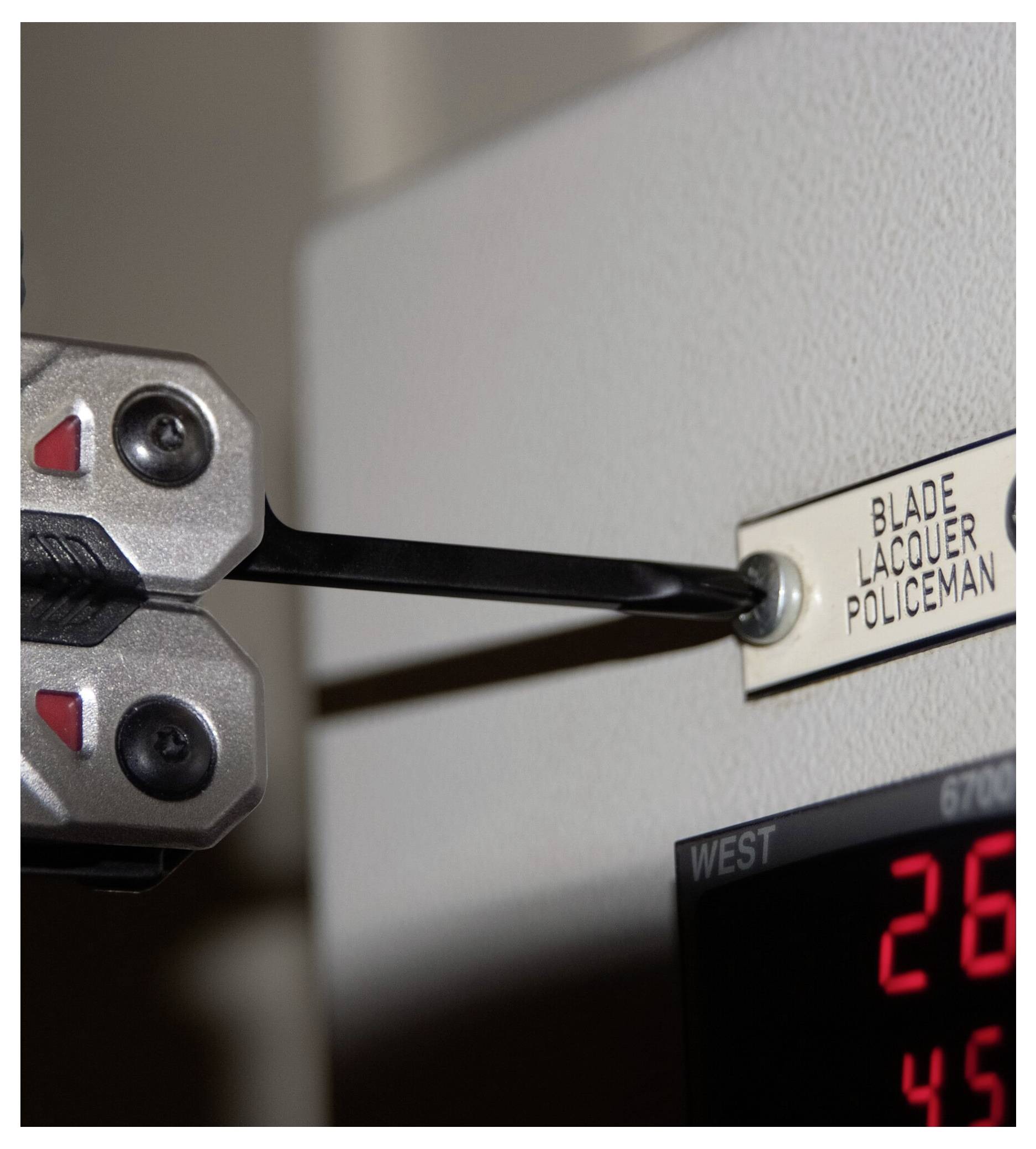 En metallverktyg är infört i ett etikettfack på en elektronisk enhet som visar siffror, med etiketten som läser "Blade Lacquer Policeman".
