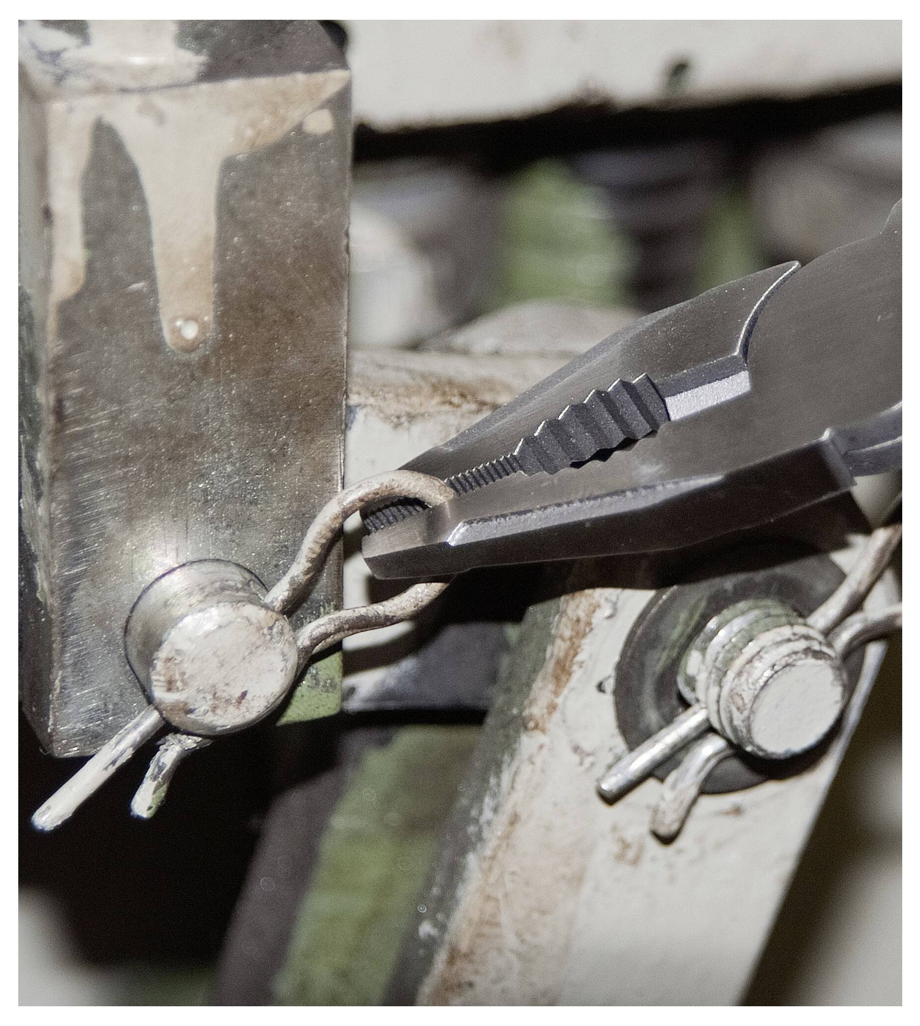 Närbild av tänger som böjer en metalltråd på en del av industriell maskineri, som visar en detaljerad vy av verktygets grepp och precision.