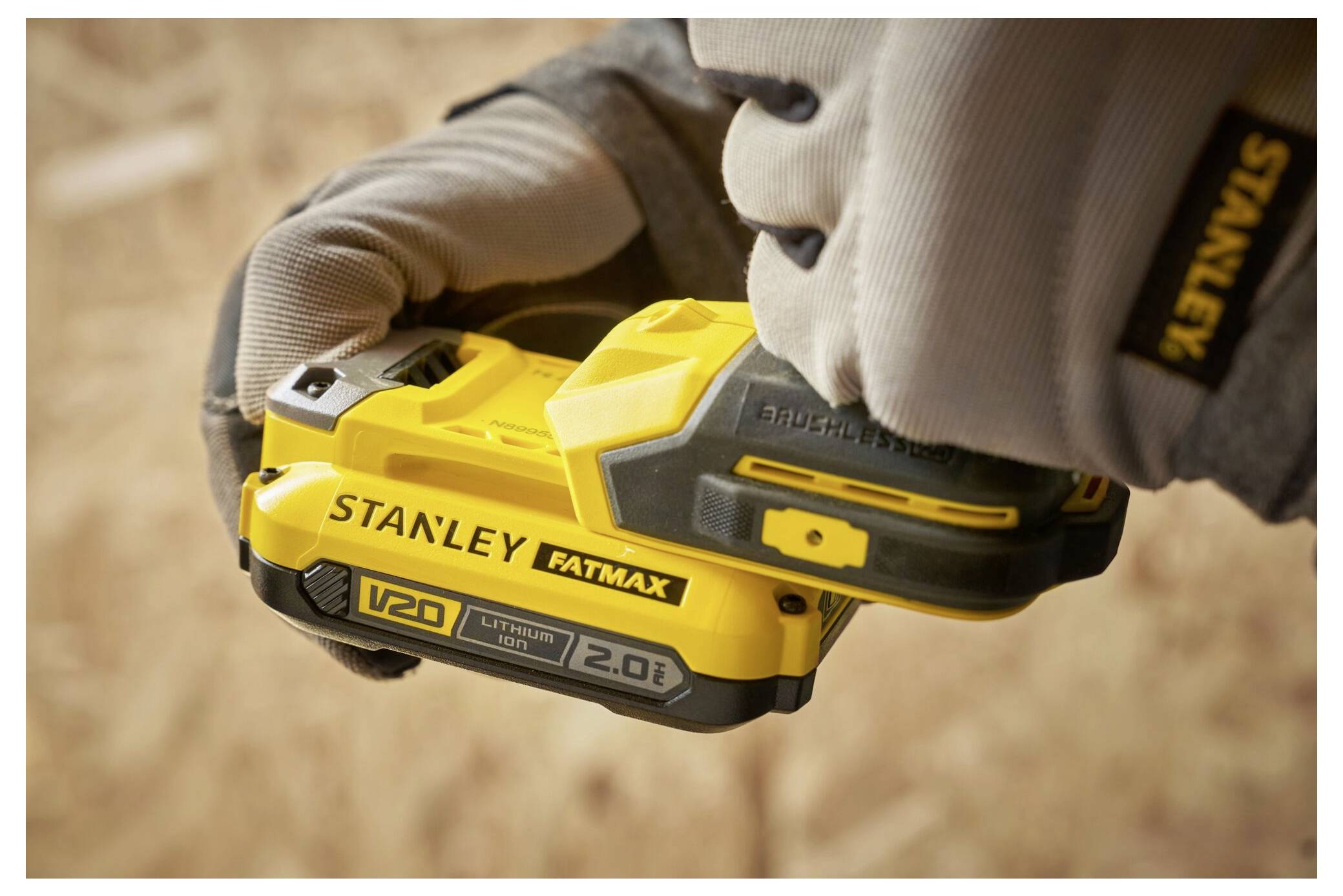 En person som håller ett gult STANLEY FATMAX 20V litiumjonbatteri och förbereder sig för att fästa det på ett verktyg. Miljön tyder på en byggarbetsplats.