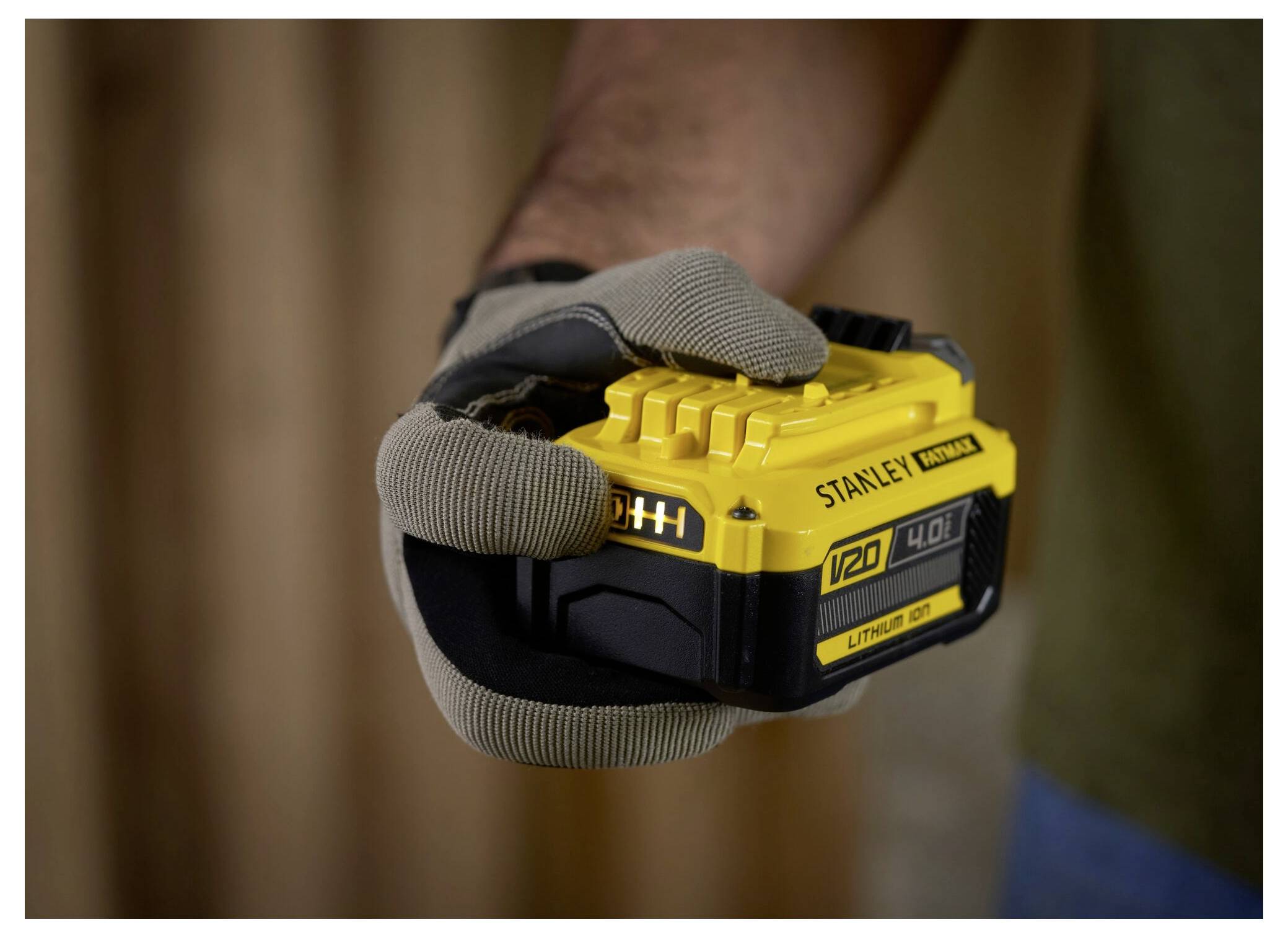 En handskad hand som håller ett gult Stanley 20V litium-jon-batteri. Bakgrunden är suddig, vilket förstärker fokus på batteriprodukten.