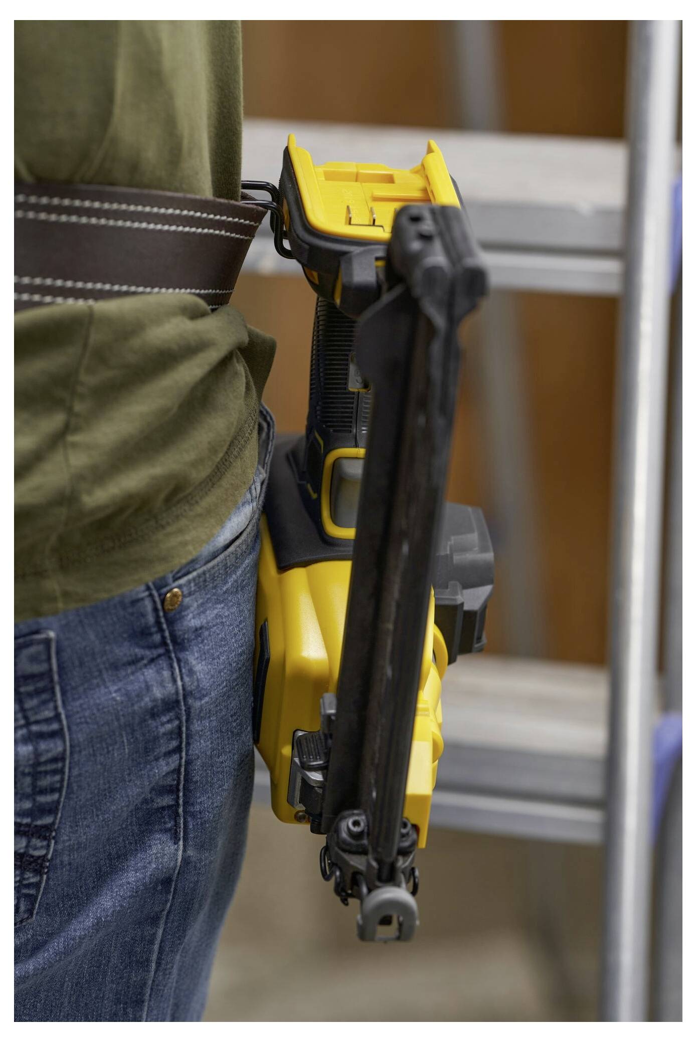 'En person som står bredvid en stege bär en gul spikpistol fäst vid sitt bälte.'