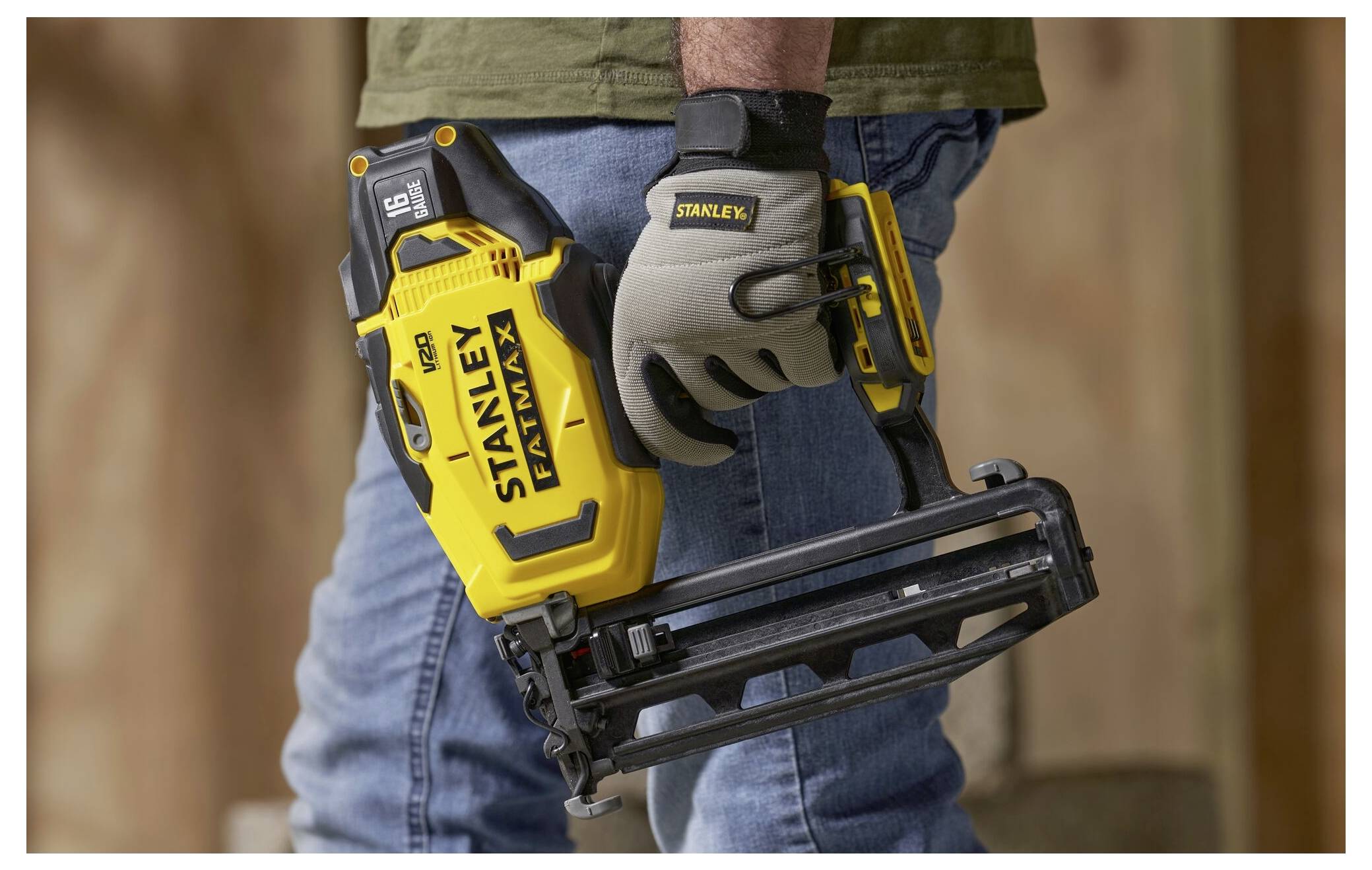 En person som bär handskar håller ett gult spikpistol i en konstruktionsmiljö, vilket belyser verktygets ergonomiska design och användbarhet.