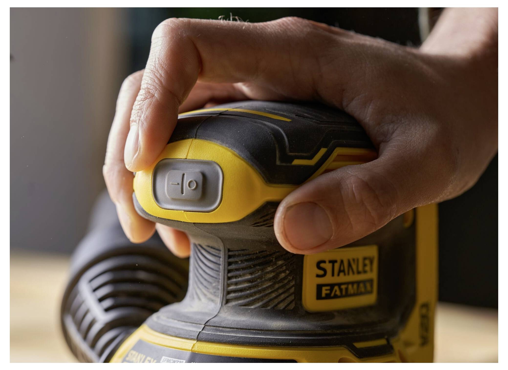 En hand som håller ett Stanley Fatmax-elverktyg, med ett finger på strömknappen, redo för användning.