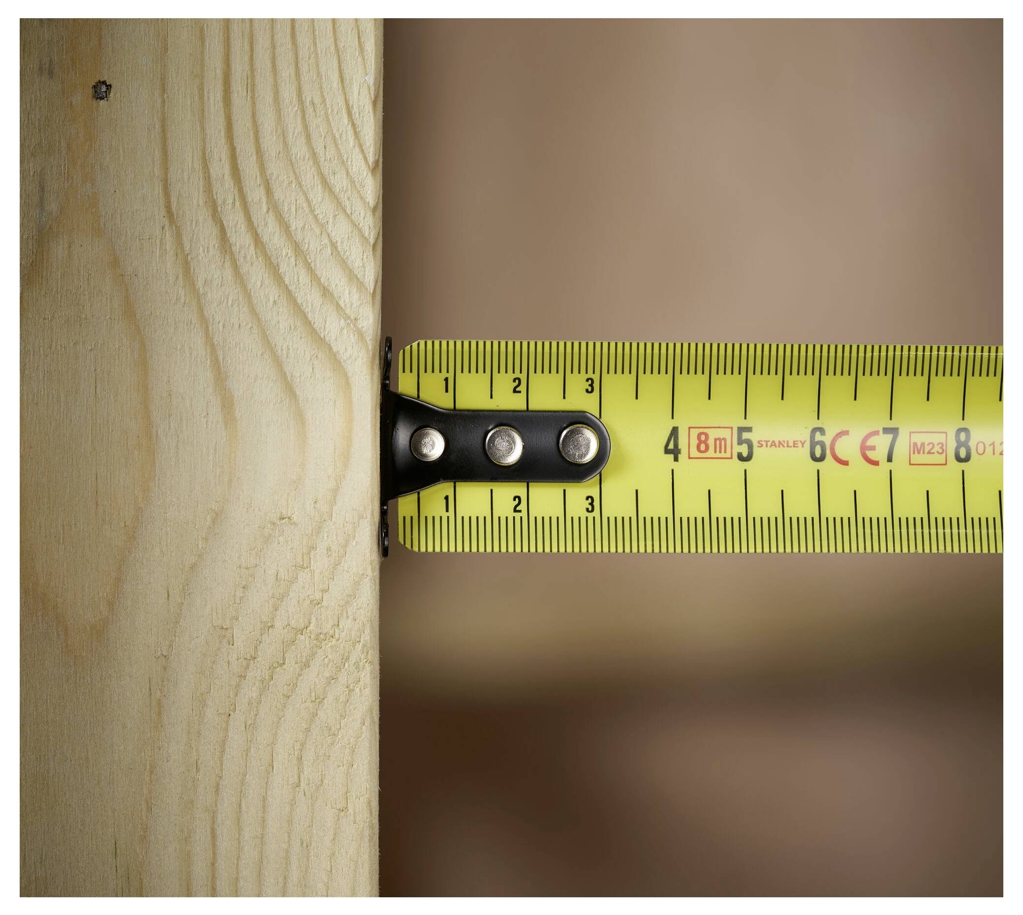 En närbild av ett gult måttband utdraget mot en träplanка, som visar en mätning på cirka 3,7 centimeter.