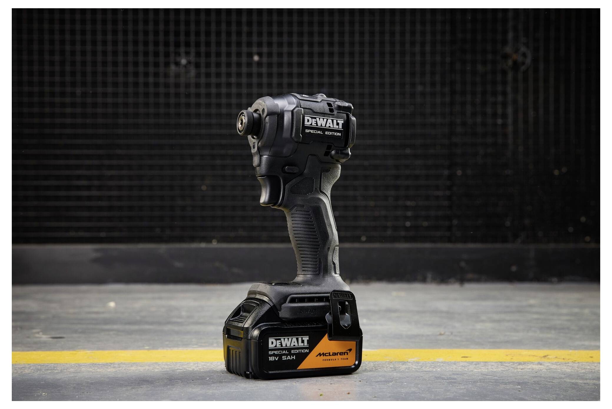 Svart DeWalt trådlös slagskruvdragare stående upprätt på en betongbotten med en gul linje, mot en mörk industriell bakgrund.