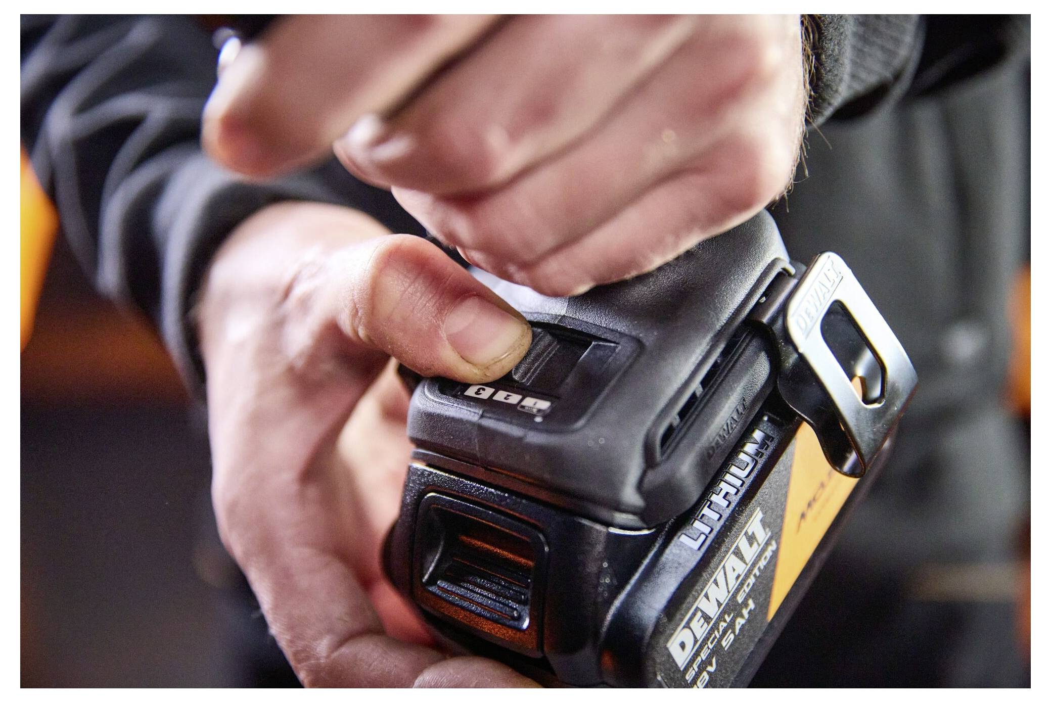 Närbild av en hand som justerar frigöringsknappen på ett DeWalt-batteripak som är kopplat till ett elverktyg.