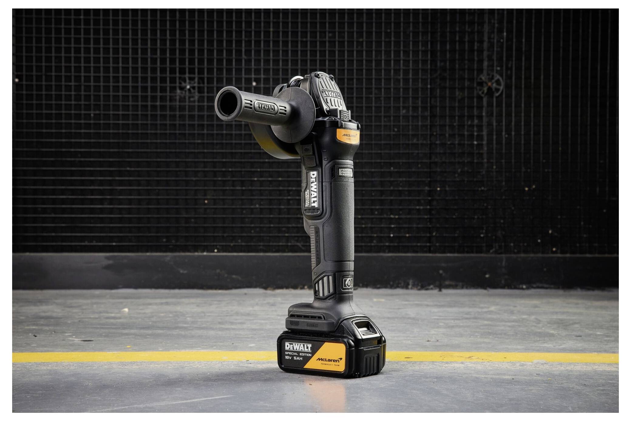 En DeWalt trådlös vinkelslipar står upprätt på ett betonggolv mot en mörk vägg, med sidhandtaget fäst.