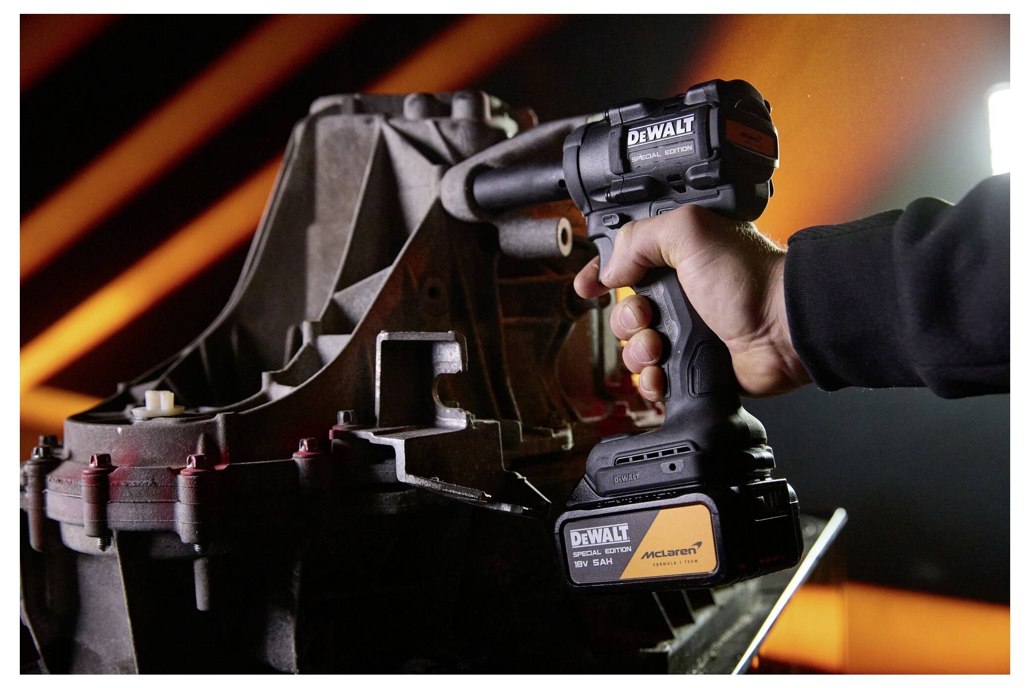 En hand använder en DeWalt trådlös slagskruvmejsel på en metallmaskin eller motorkomponent i en verkstadsmiljö.
