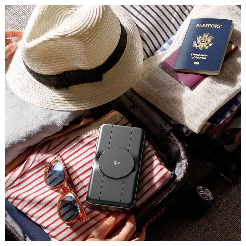 Packade resegods staplade på kläder: halmhatt, amerikanskt pass, solglasögon och en kompakt Qia-enhet, vilket tyder på förberedelser för en resa.