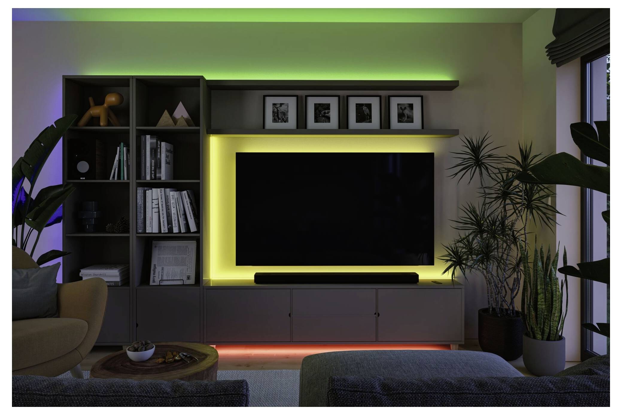 Modernt vardagsrum med mediaväggen med stor TV, belyst av grön, gul och orange LED-accentbelysning, flankerad av hyllor, växter och skåp.