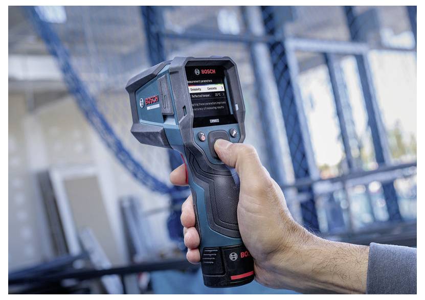 Hand som håller en Bosch värmekamera riktad mot en industriell struktur, med enhetens skärm synlig som visar ett mätgränssnitt.