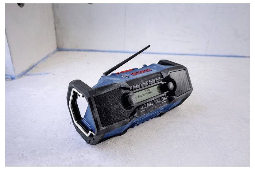 En blå och svart bärbar Bosch-radio står på en vit yta mot en slät vägg, med sin antenn upphöjd.
