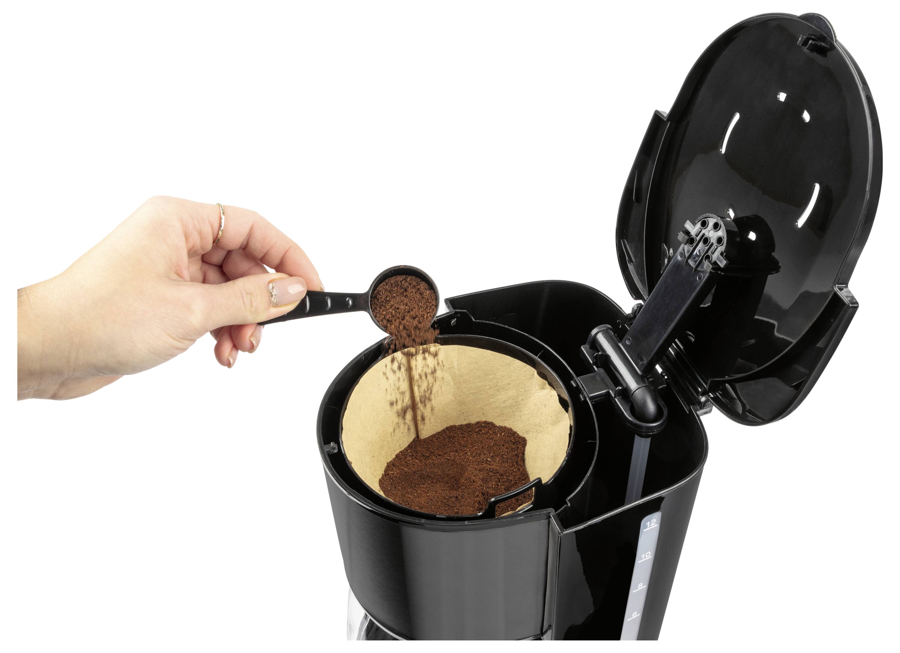 Hand hälls malet kaffe från en skopa in i en öppen svart kaffebryggare med ett papperfilter inuti.