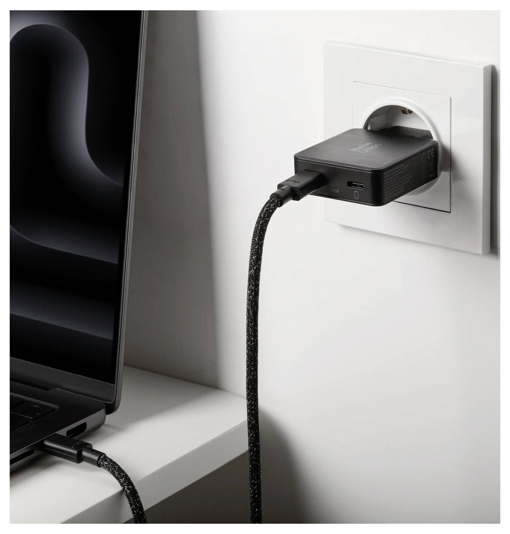 Bärbar dator som laddas från ett vägguttag via en svart adapter inkopplad i uttaget, med en kabel ansluten till den bärbara datorn och en annan hängande ner.