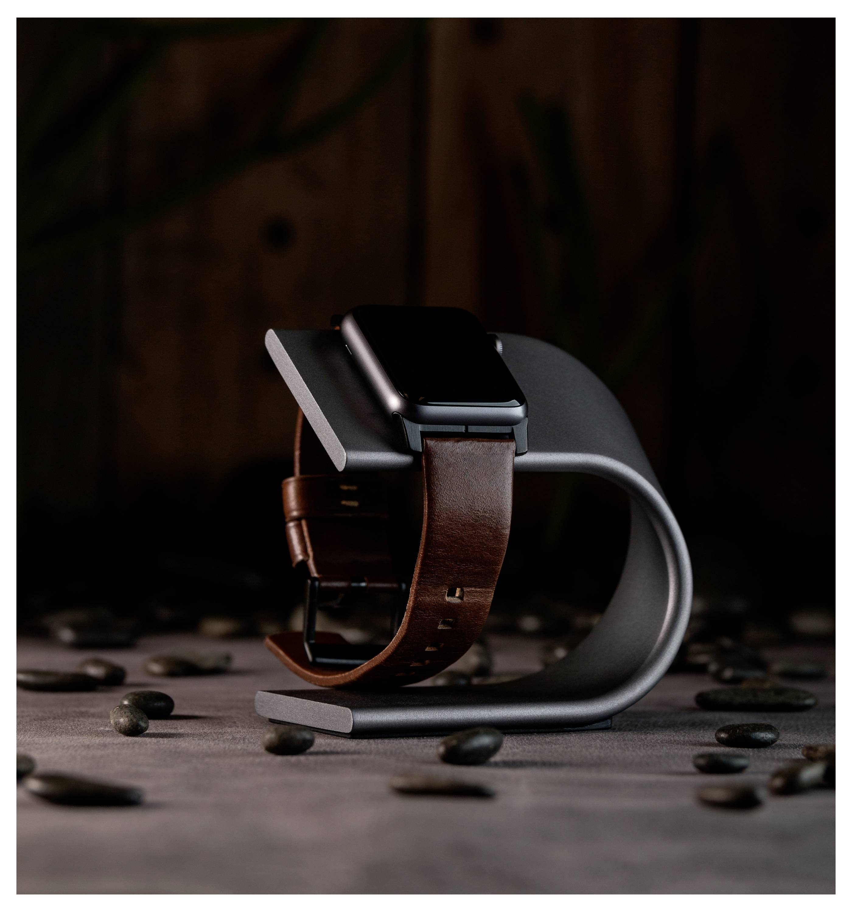 Smartwatch med brunt läderband på en böjd ställning, omgiven av kaffebönor på en mörk bord.